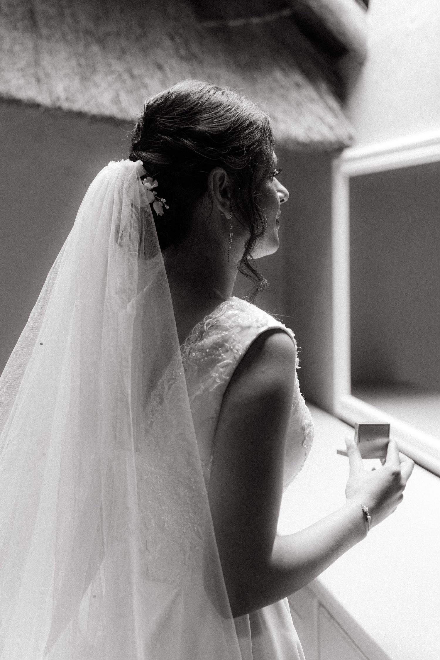 A bride in a white wedding dress and long veil gazes away from camera in black and white portrait.