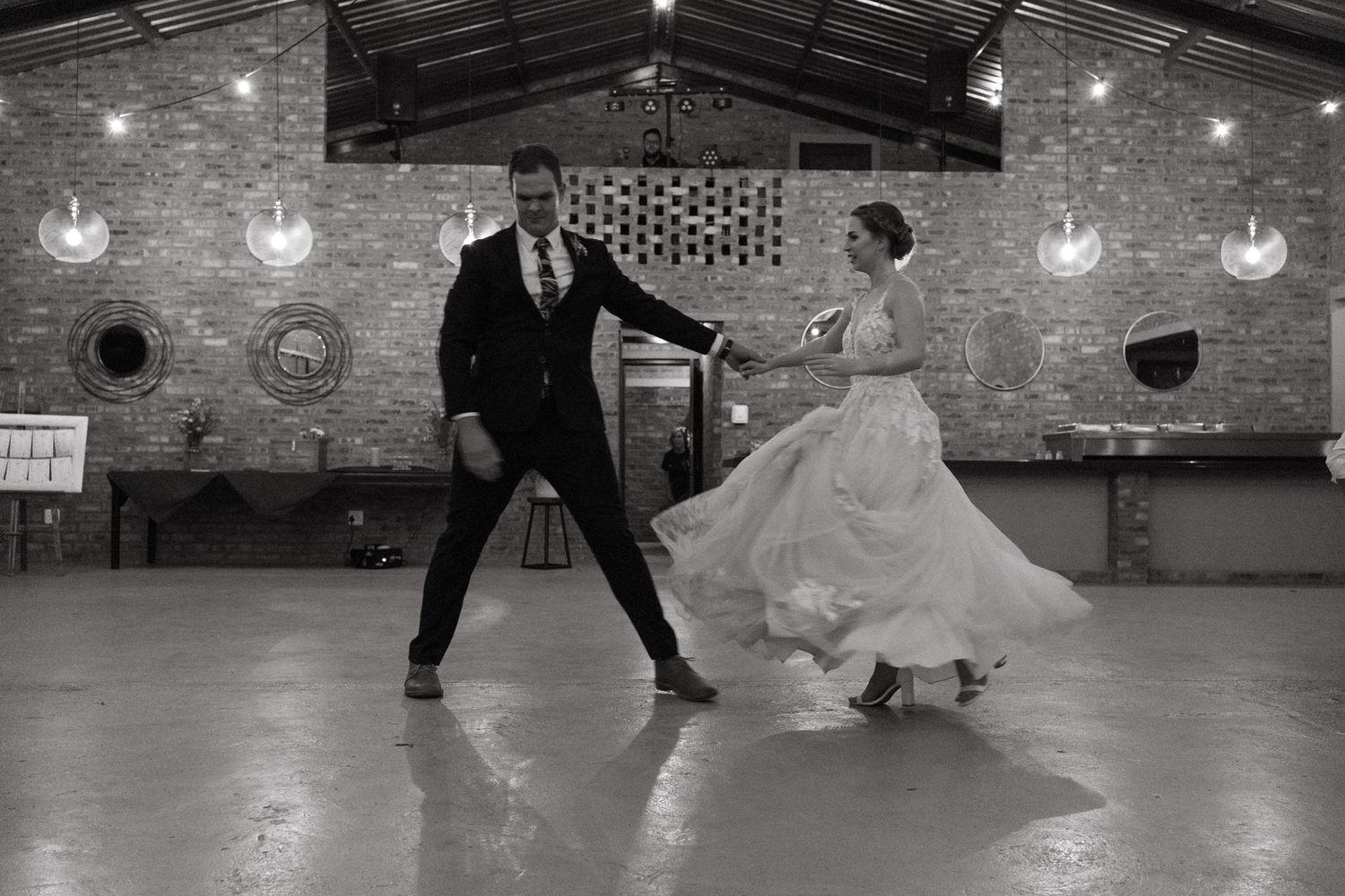 Black and white capture of a joyful wedding dance in an industrial-style reception venue.