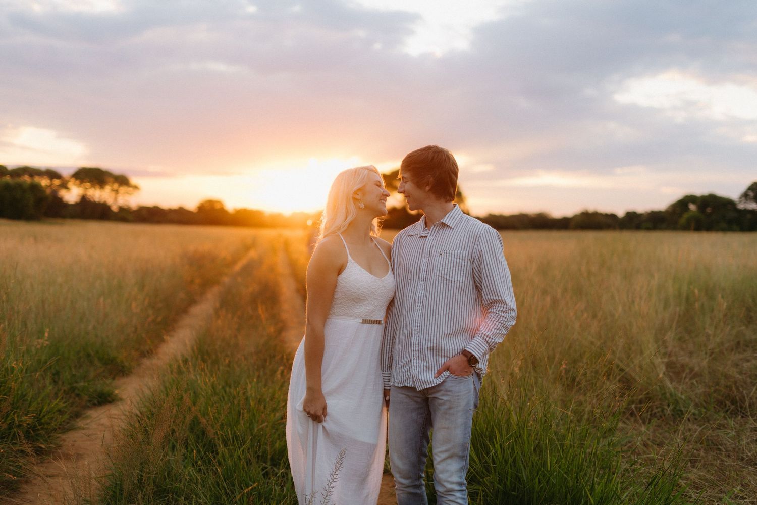 A couple walking hand in hand through a golden field at sunset.