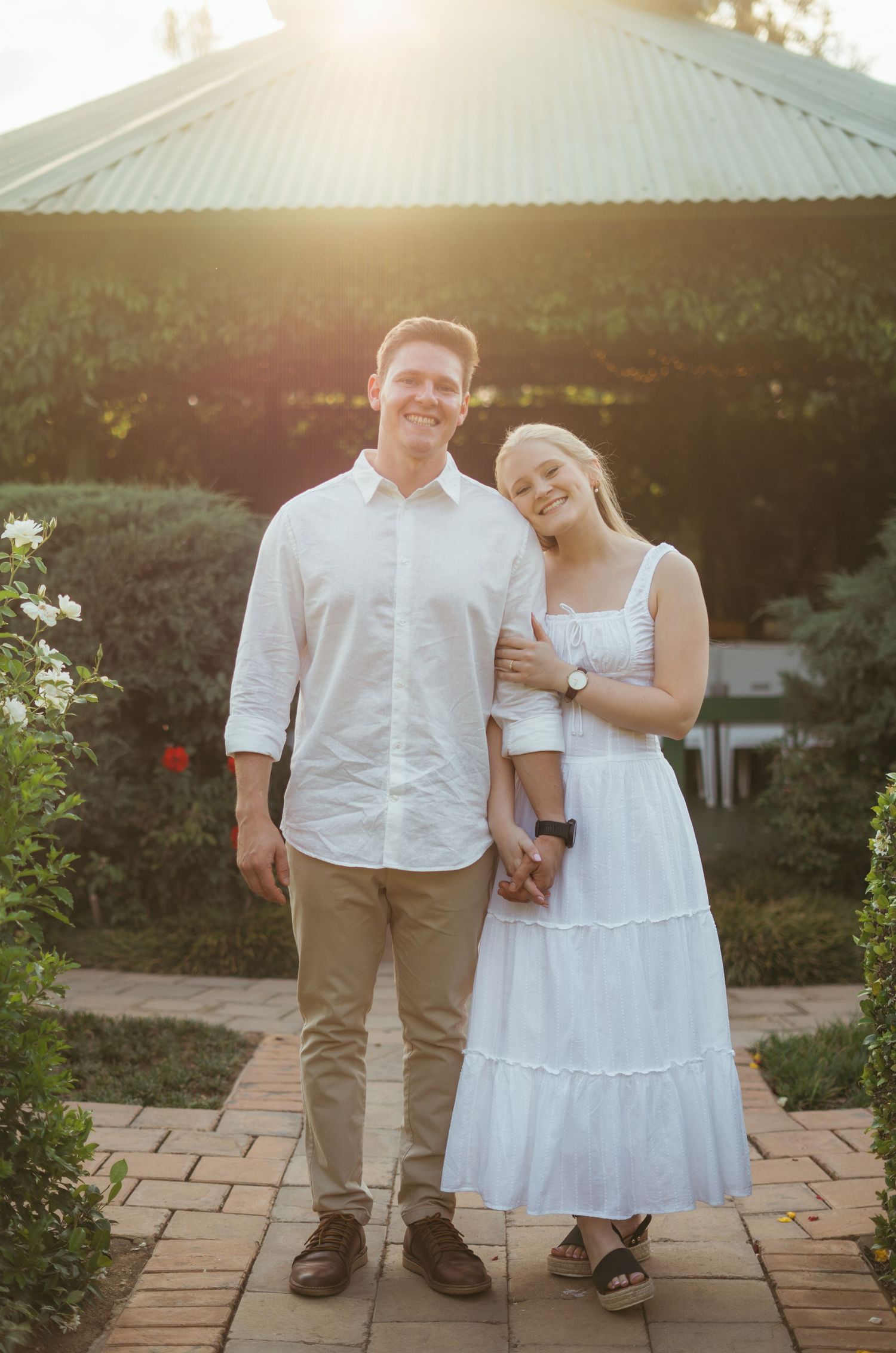 Couple in coordinated white outfits standing together on stone patio at sunset.