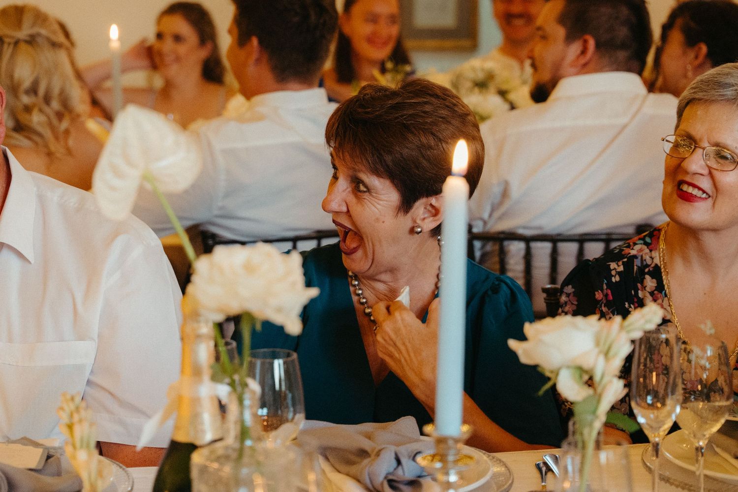 A candlelit dinner party scene shows people laughing and enjoying conversation at a formal table setting.