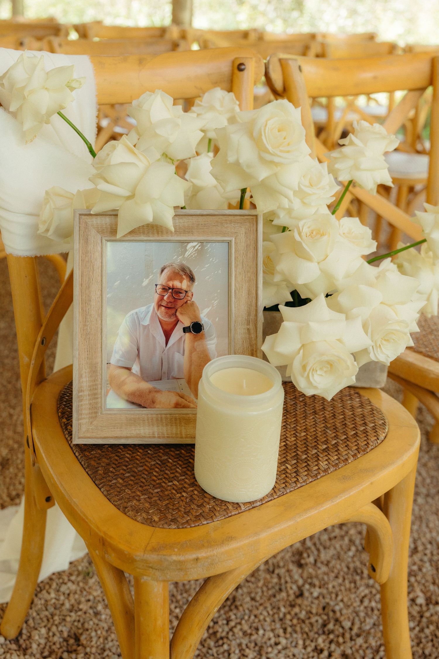 Memorial display with white lilies and framed photographs arranged on wooden chairs with woven seats at a celebration event.