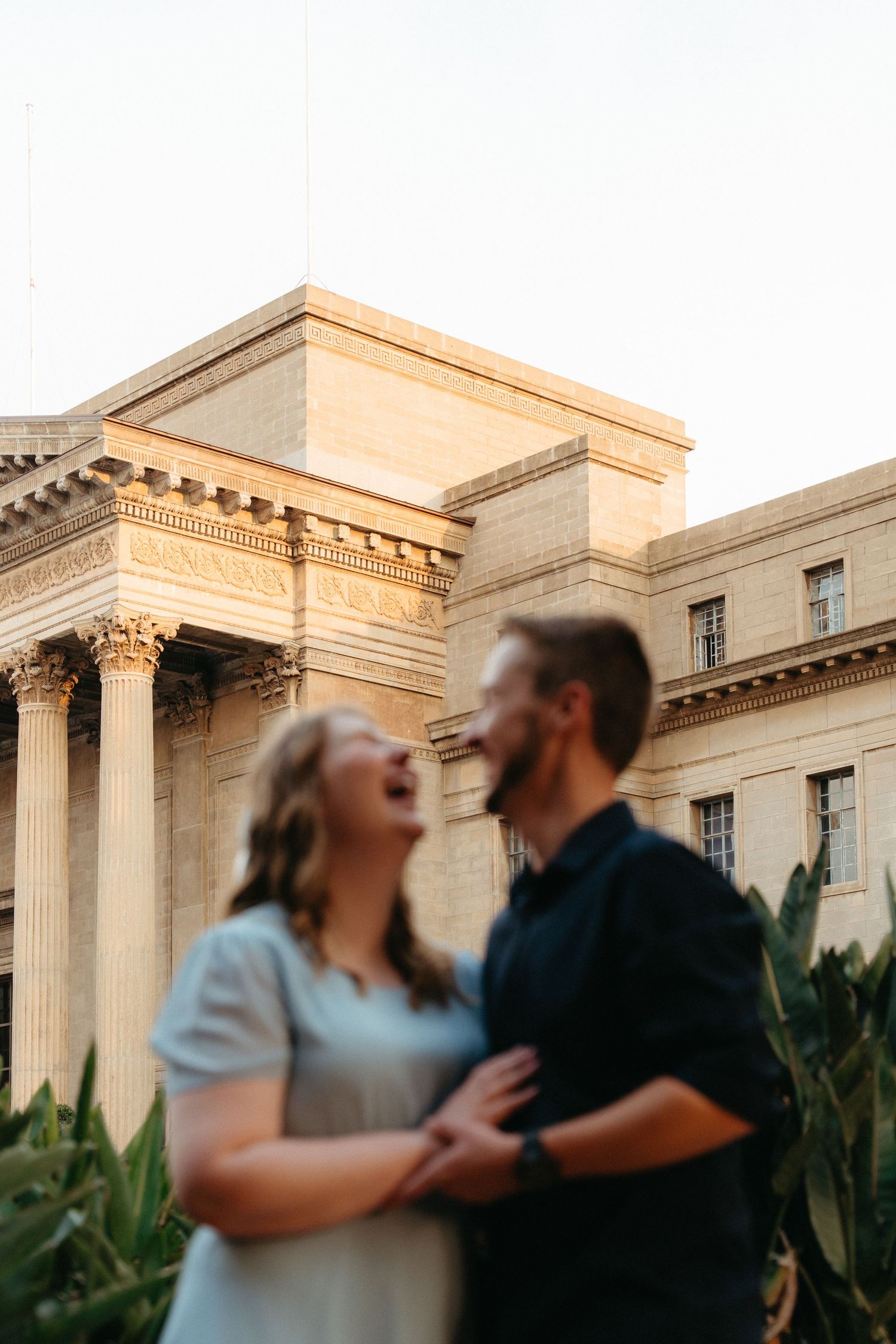 A couple shares a joyful moment together outside a grand neoclassical building with columns during golden hour.