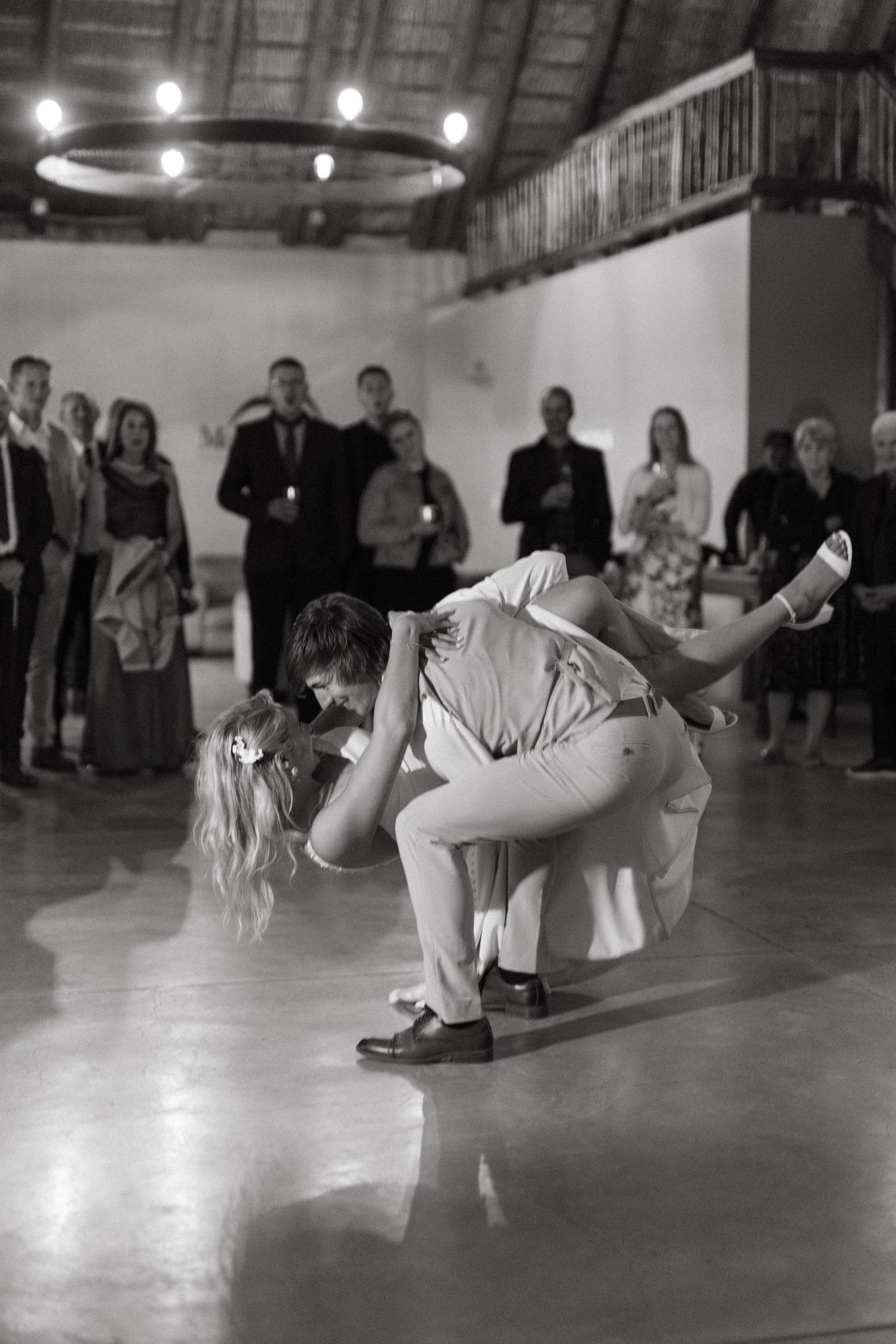 Couple performs dramatic dip during first dance at wedding reception at Mountain View Game Lodge while guests watch.