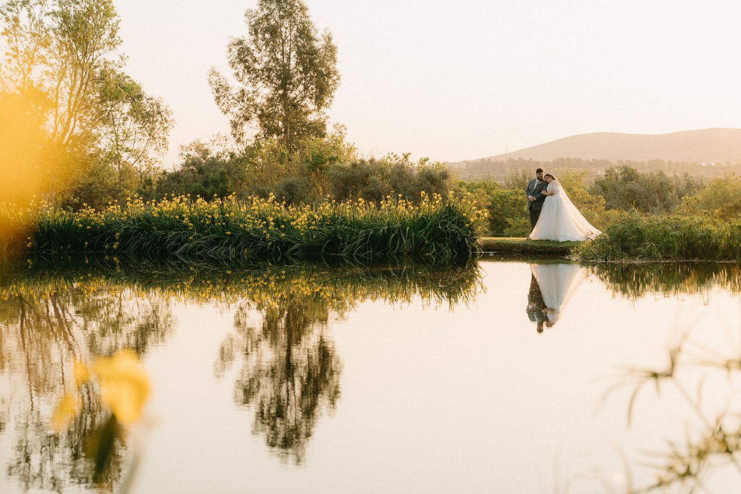 Wedding couple embraces by a reflective pond in Muldersdrift at golden hour sunset.