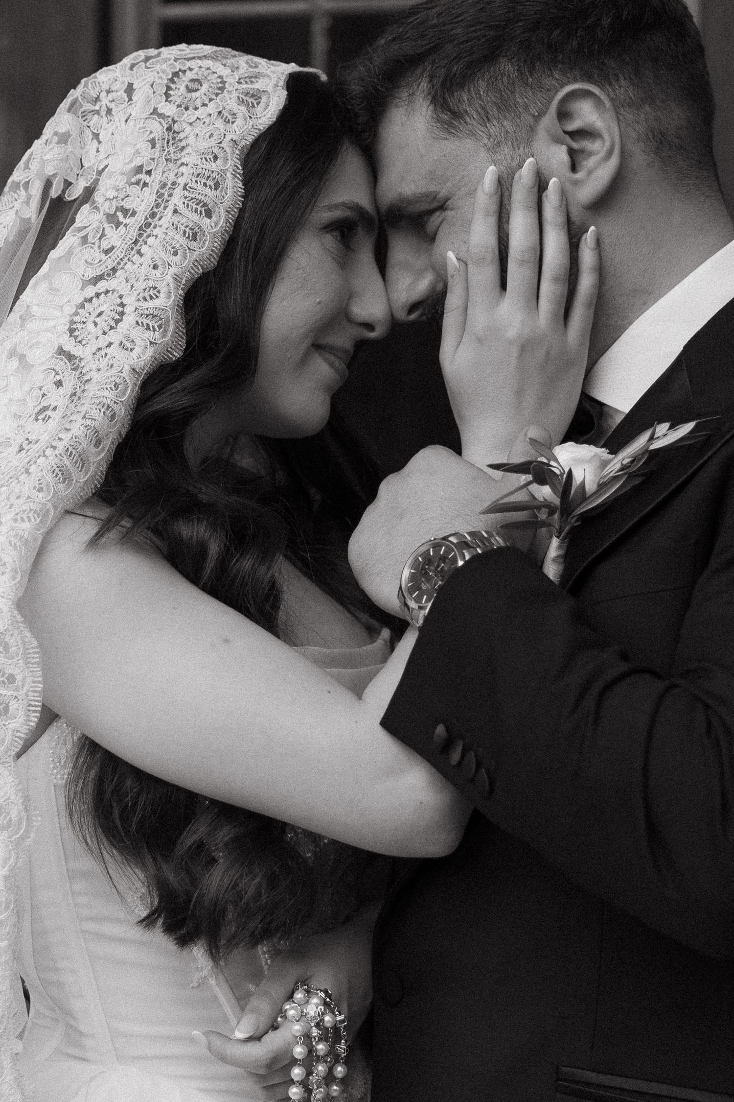 Black and white wedding photo of bride and groom sharing an intimate moment, bride wearing lace veil.