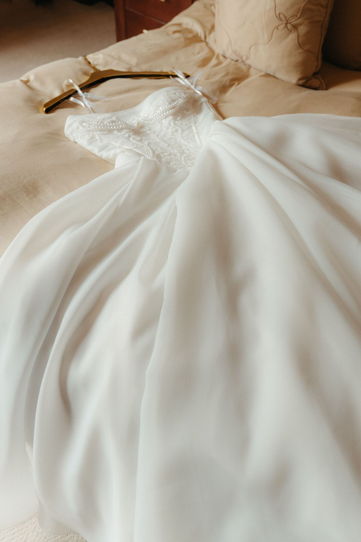 Elegant white ball gown wedding dress with lace bodice displayed on a wooden hanger over a cream bedspread.