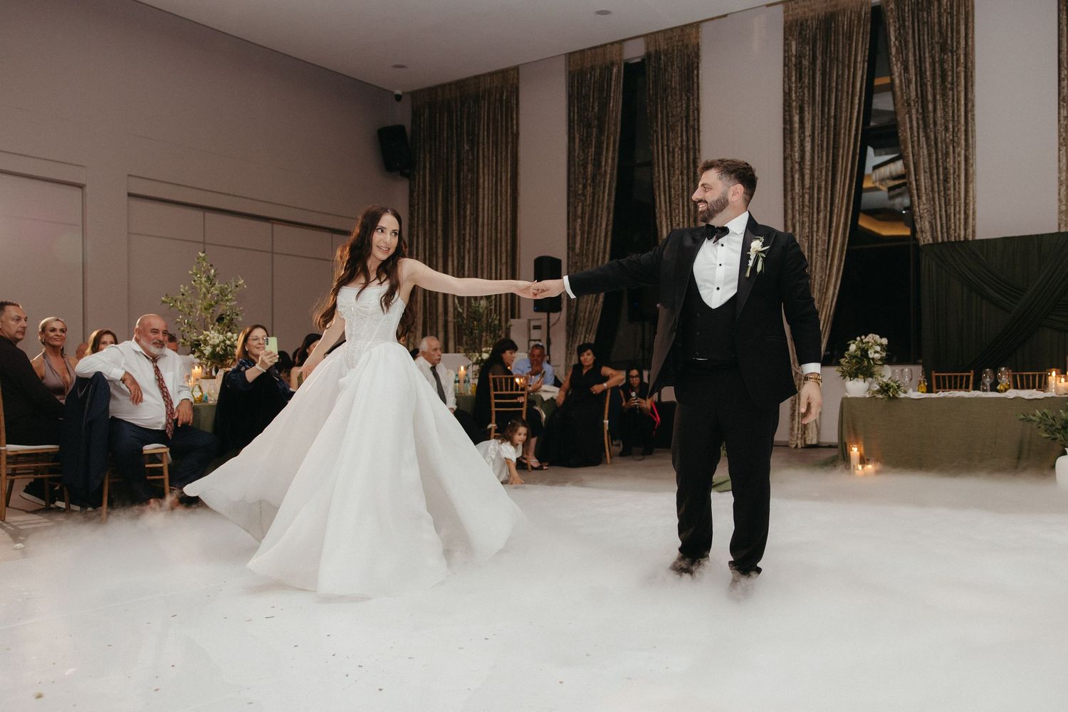Bride and groom share their first dance on a white dance floor at an elegant wedding reception venue.