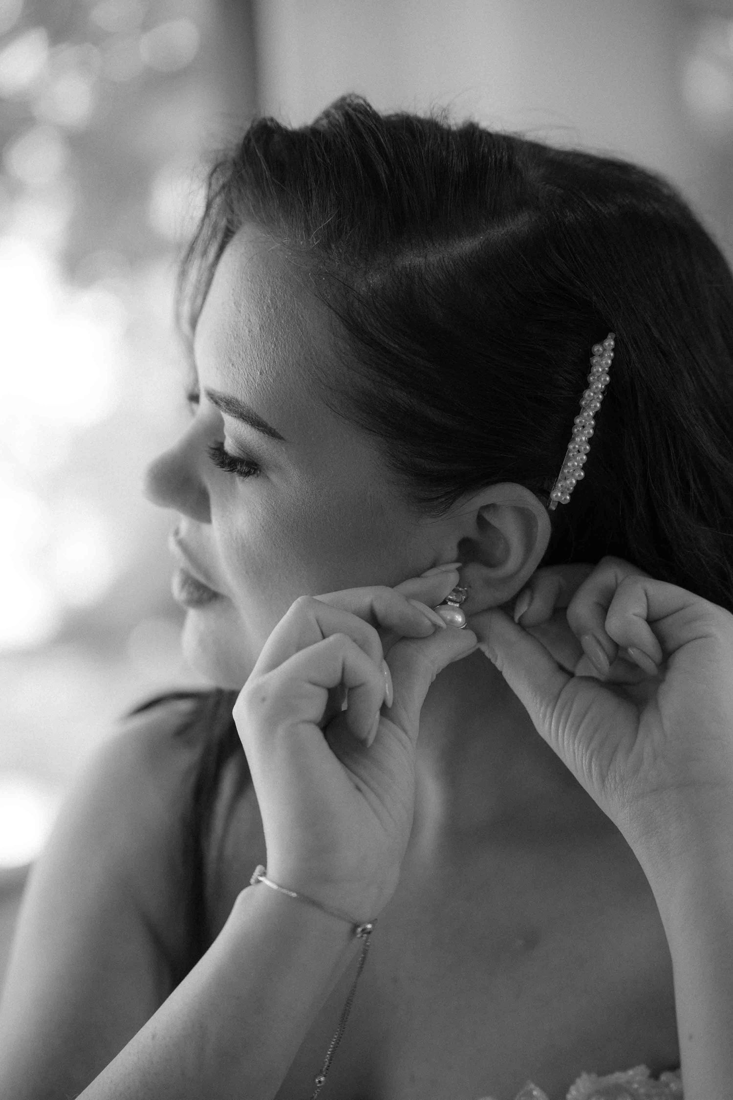 Black and white photo of a bride putting on earrings with hair clip, getting ready for her wedding day.