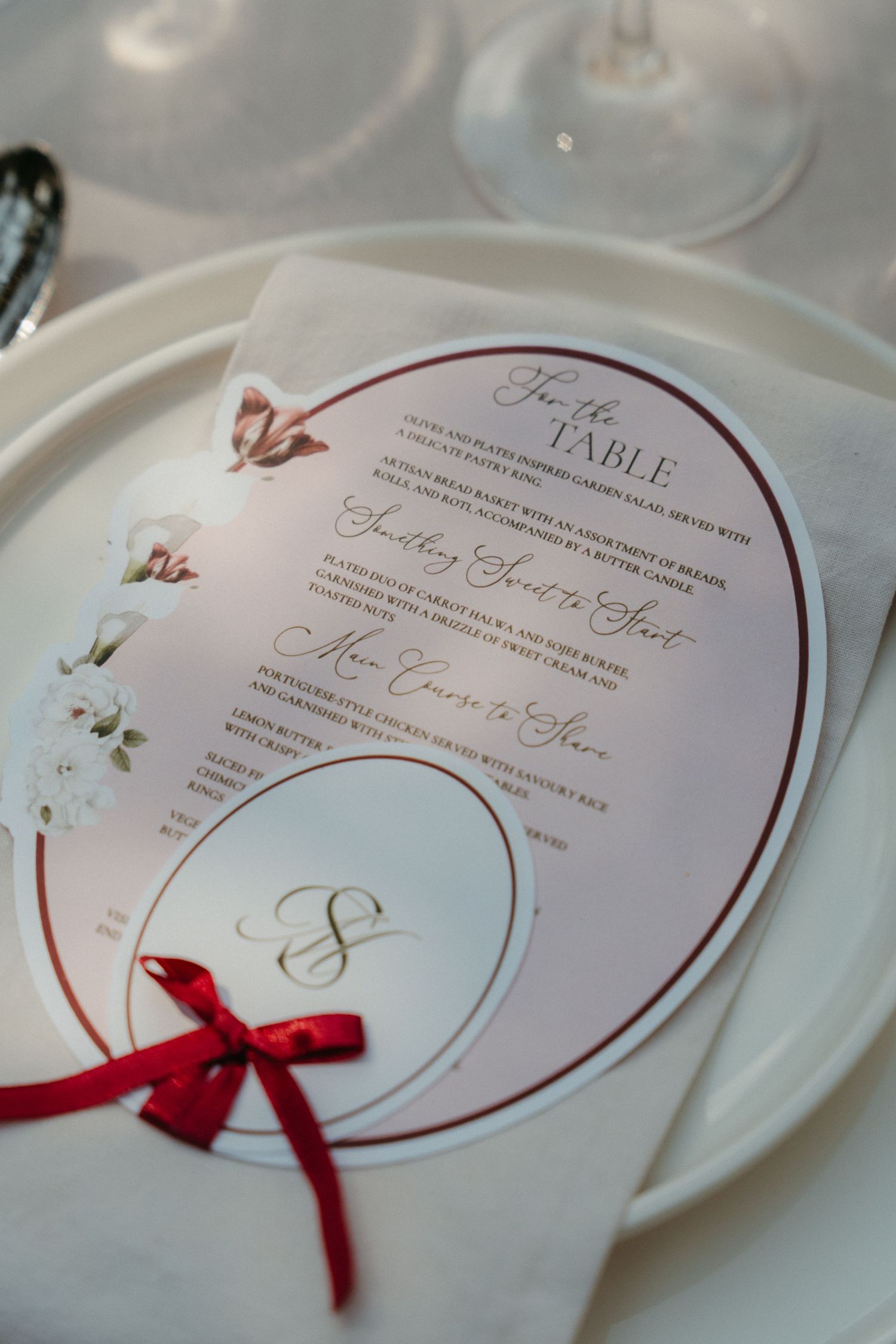 Elegant wedding menu card with red bow, monogram, and floral details on white plate setting.