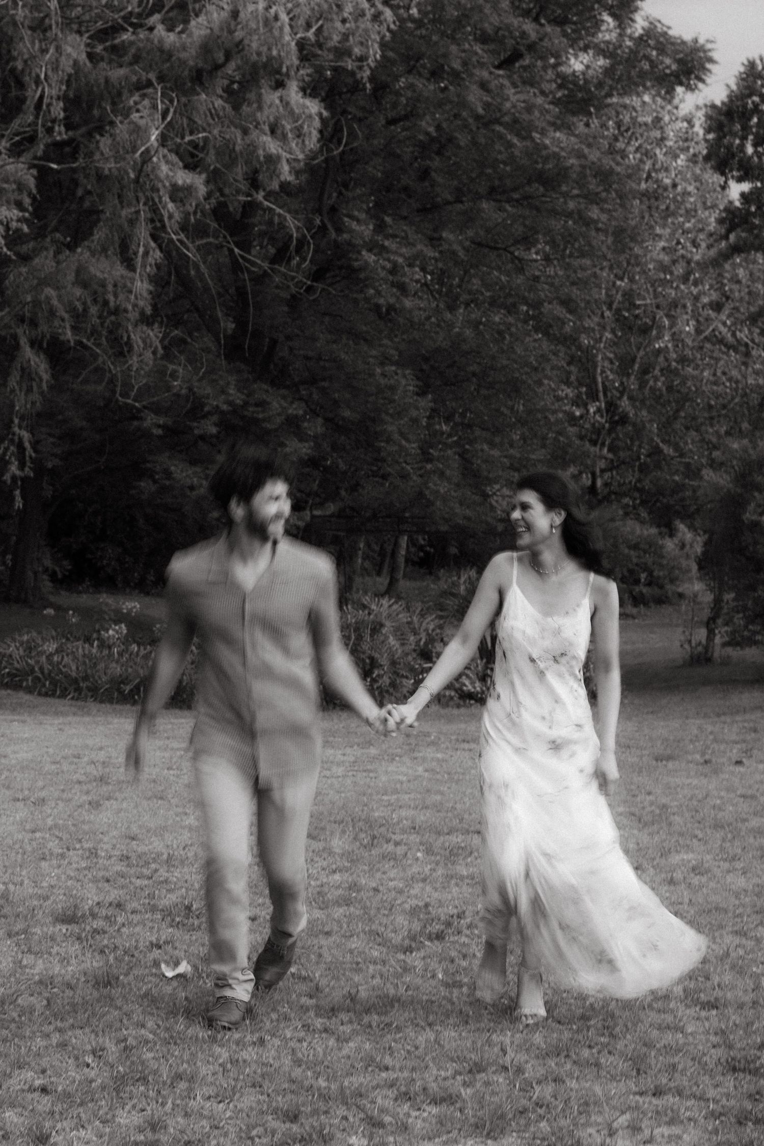 Black and white photo of couple walking hand in hand through a park.