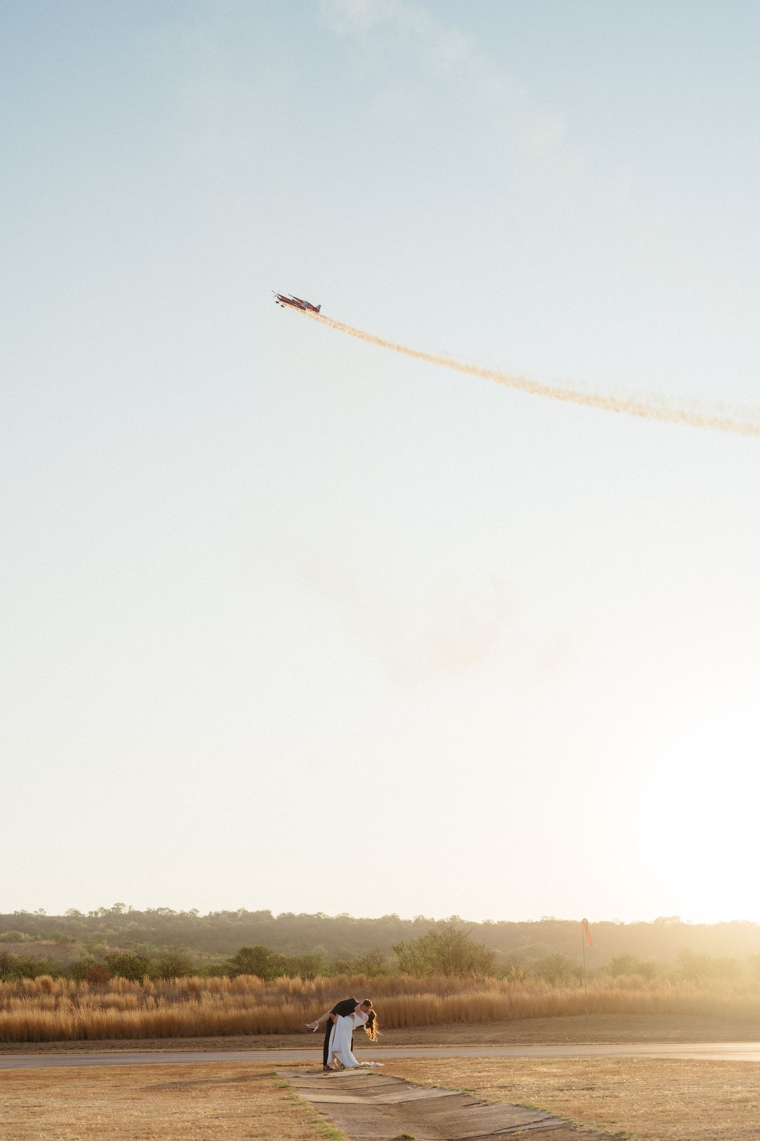 A dramatic sunset photo with an airplane trail in the sky above a couple.