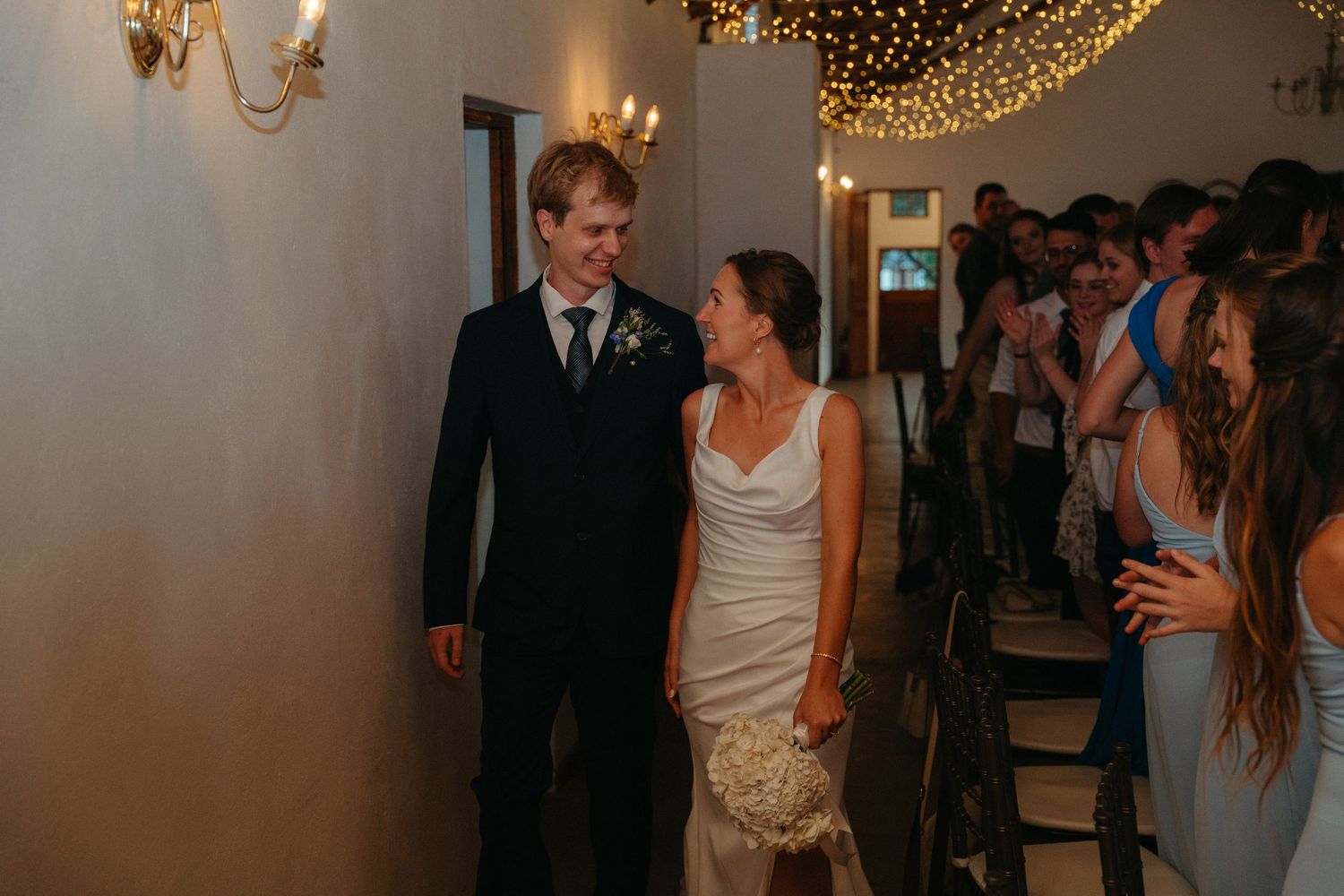 A wedding celebration with string lights overhead and guests dancing on the dance floor at an evening reception.
