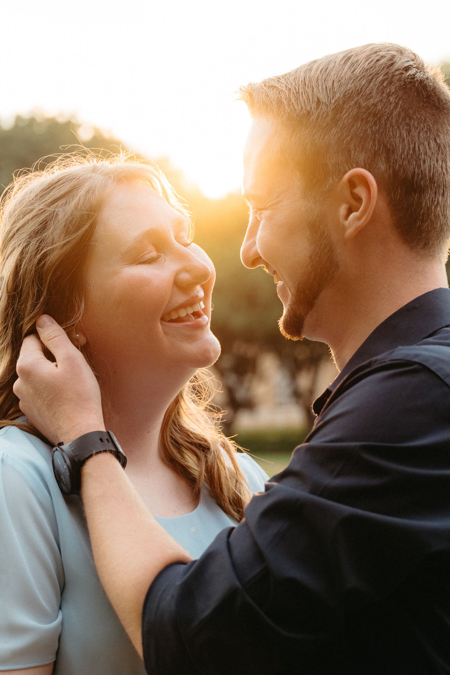 A couple shares an intimate moment while laughing together in warm sunset lighting.