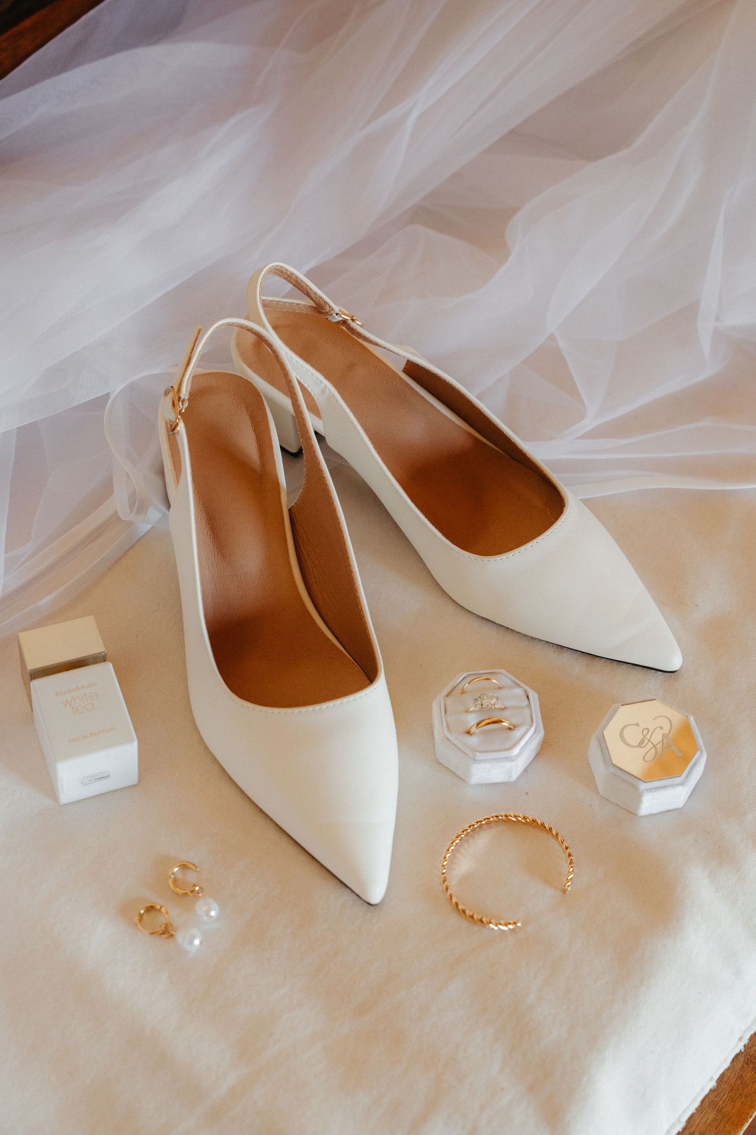 Elegant white slingback heels with pointed toes displayed alongside delicate pearl jewelry on soft tulle fabric.
