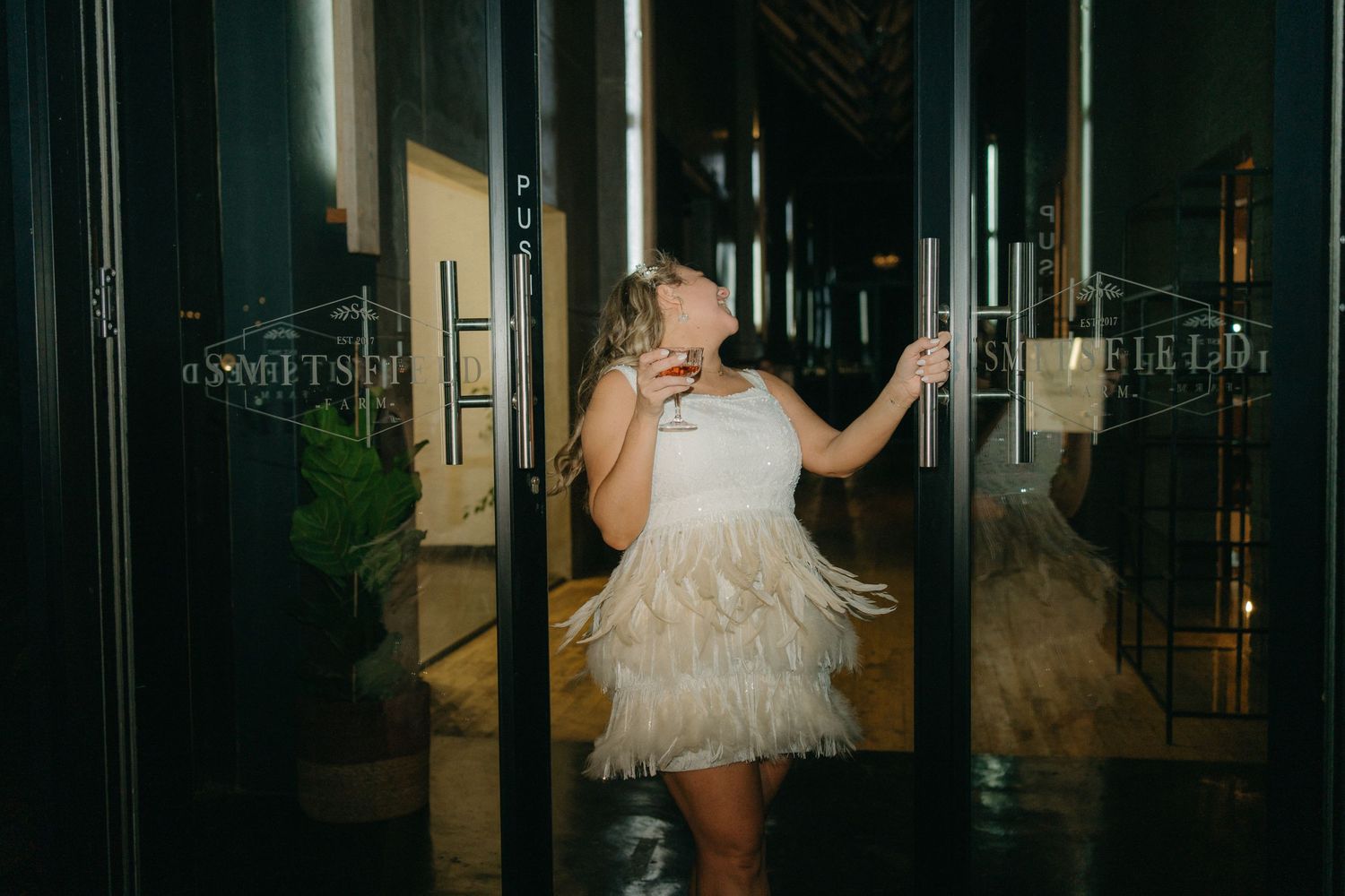 A person in a white ruffled dress poses dramatically between reflective pillars.