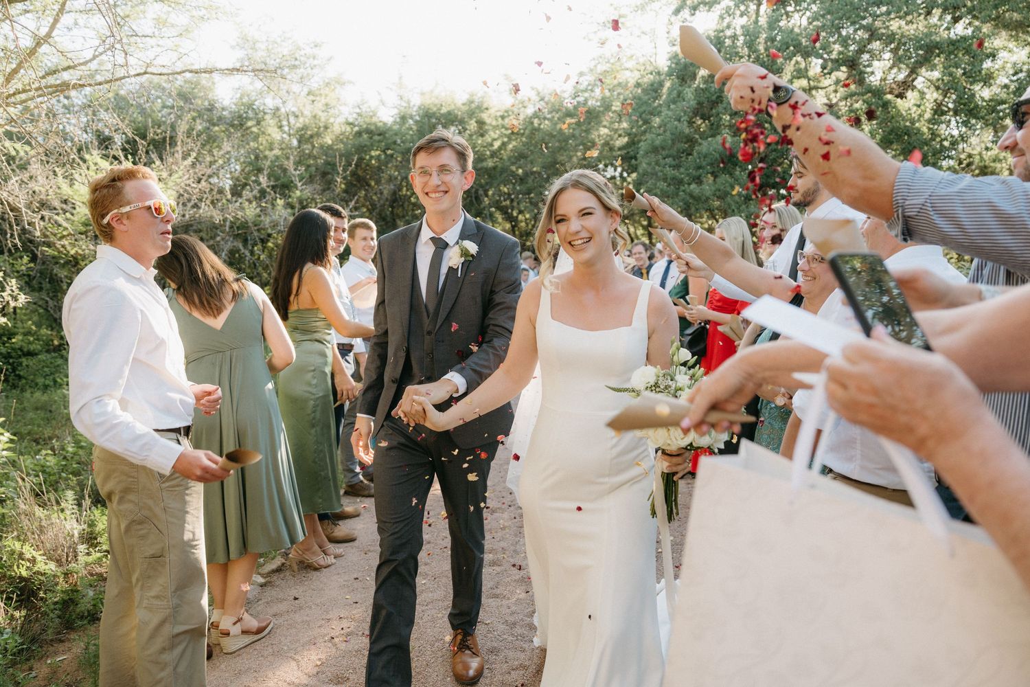 Wedding guests line a pathway throwing petals as the newlyweds walk through during their celebration.