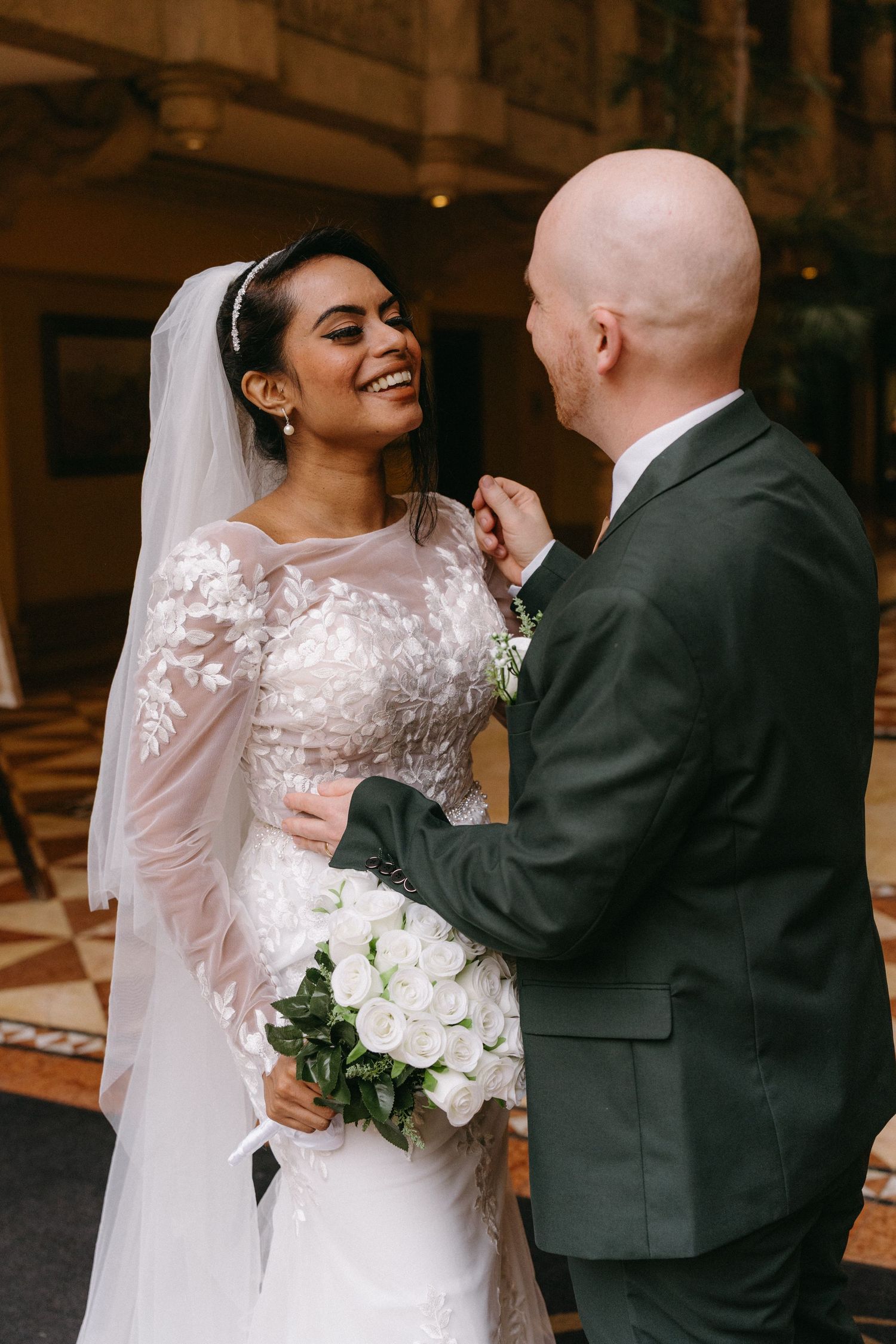 A joyful moment captured between newlyweds in an ornate indoor venue with bride holding white roses.