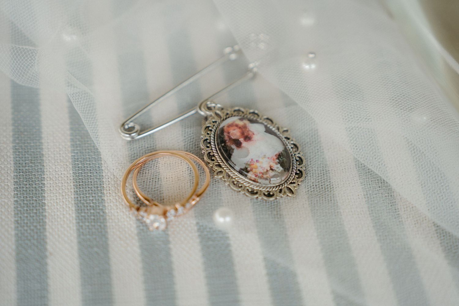 Vintage cameo brooch and delicate rose gold ring displayed on soft striped fabric with veil overlay.