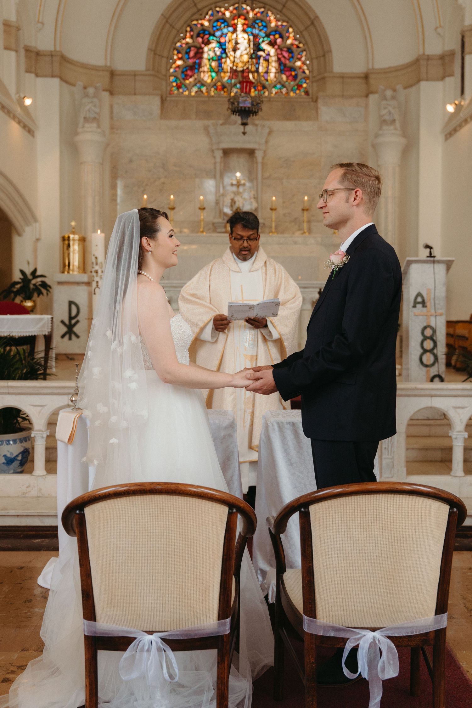 A wedding ceremony takes place inside Nazareth House Chapel with stained glass windows and ornate architectural details.