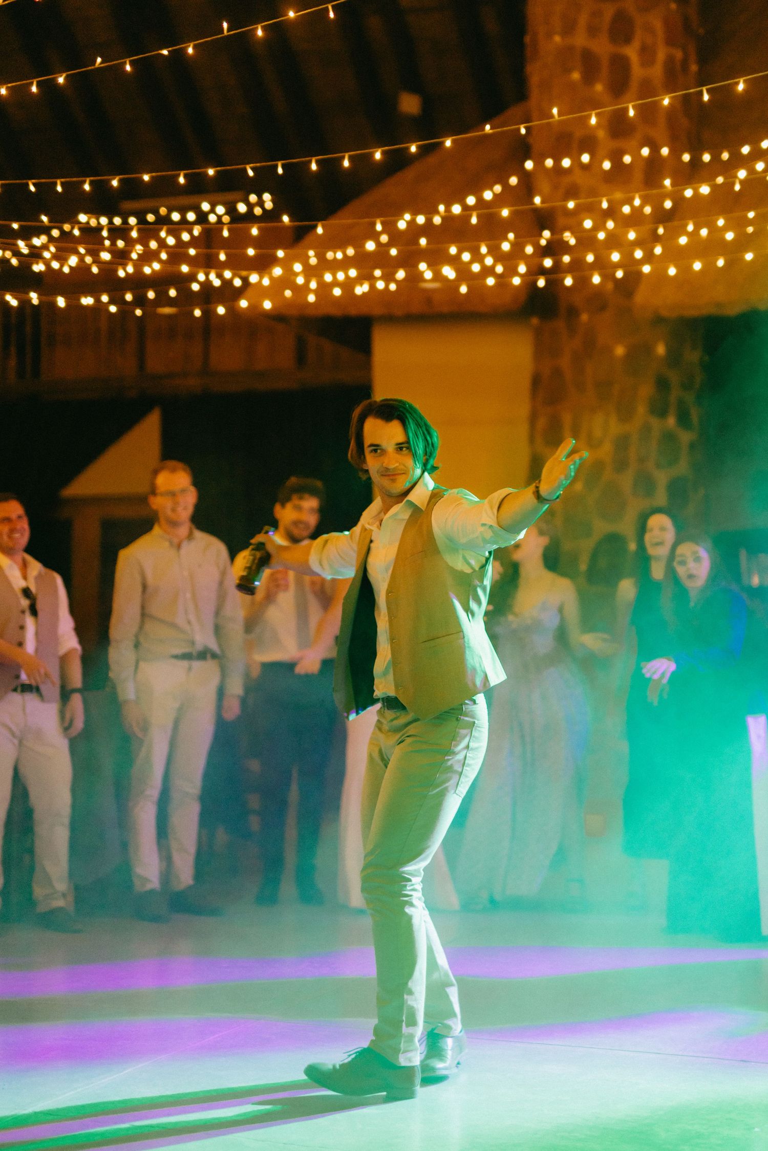Wedding reception dance floor with string lights and green ambient lighting.