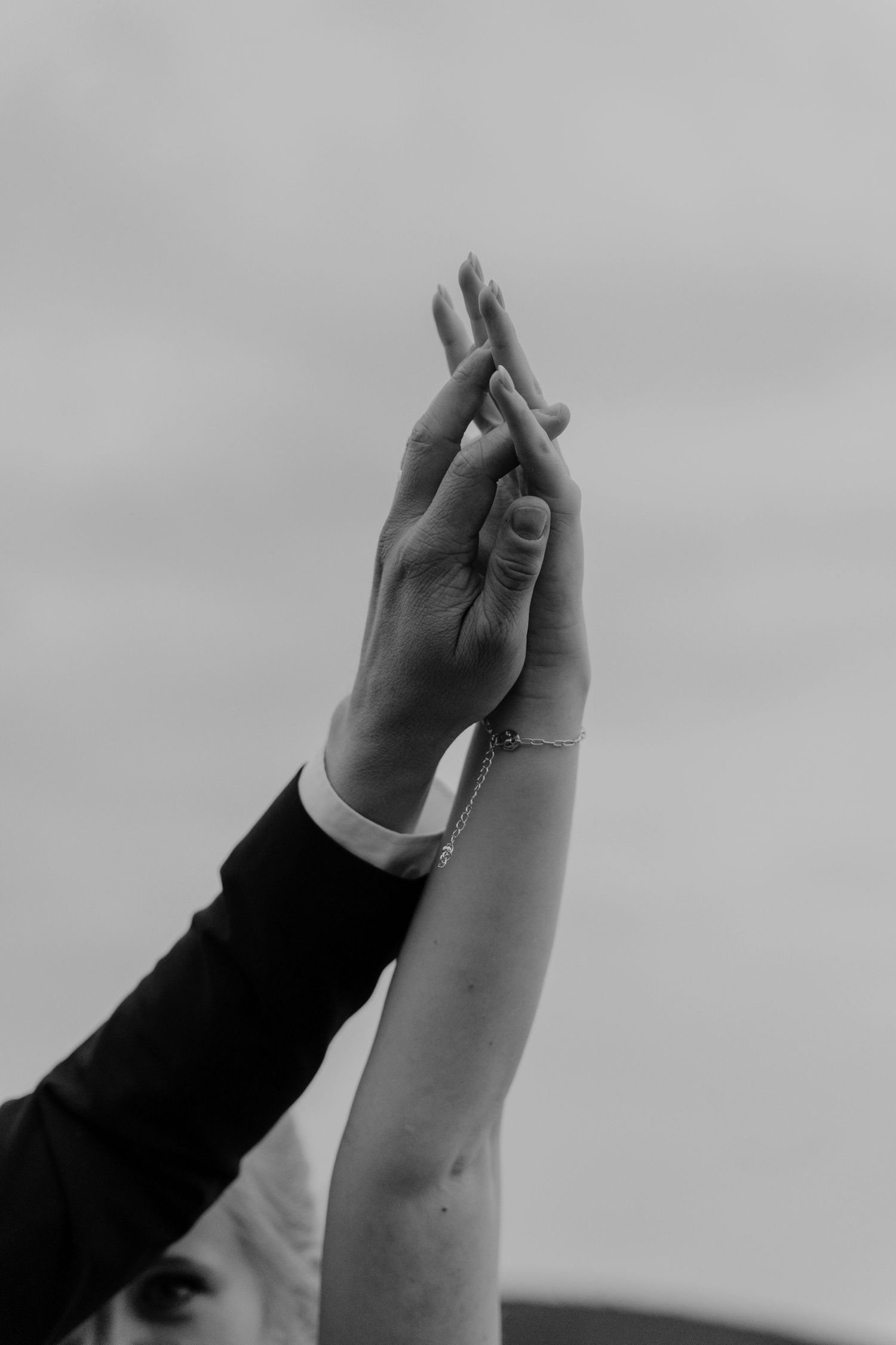 Black and white close-up of raised hands touching against a cloudy sky.
