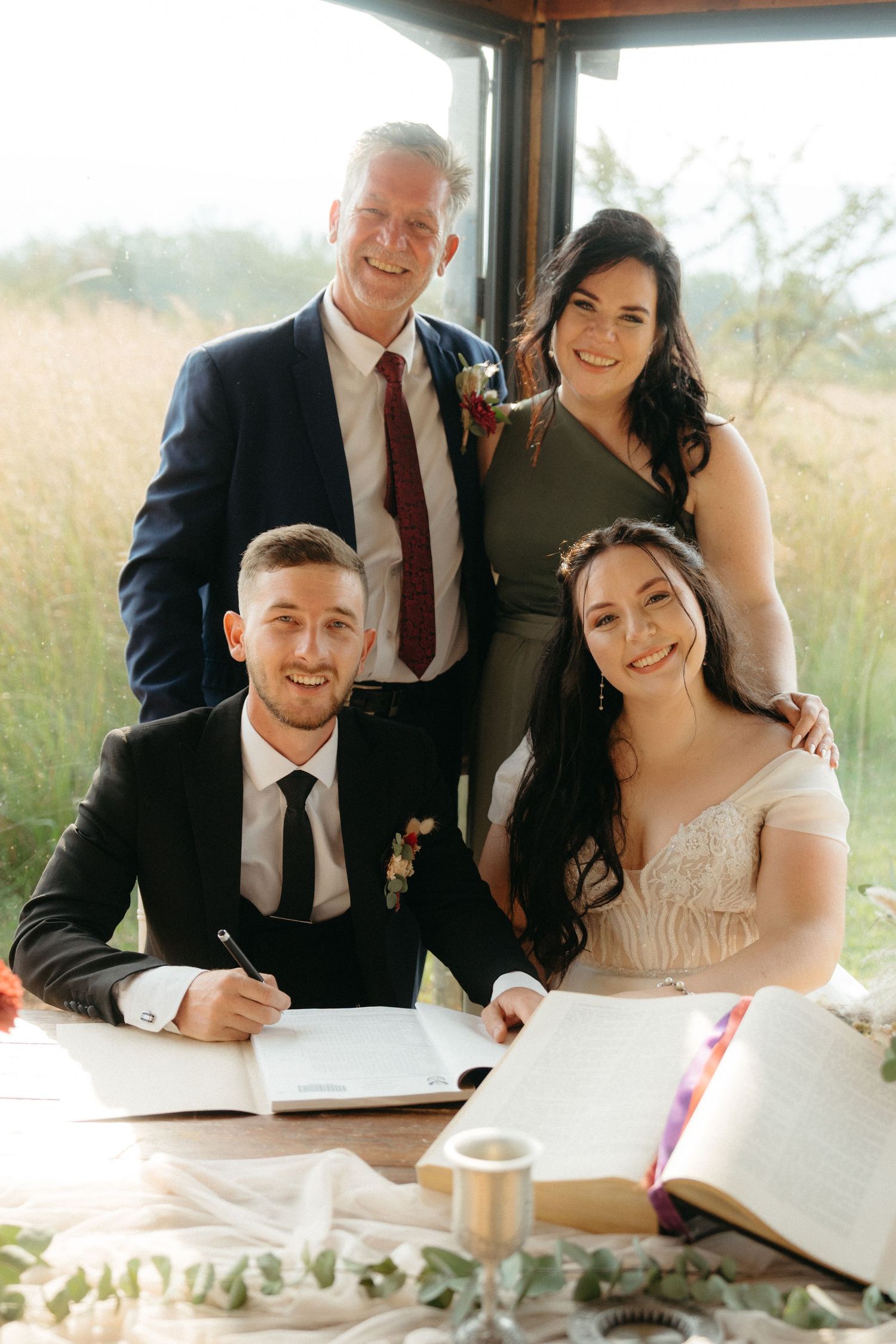 A small group gathers around a table signing wedding documents during an outdoor ceremony.