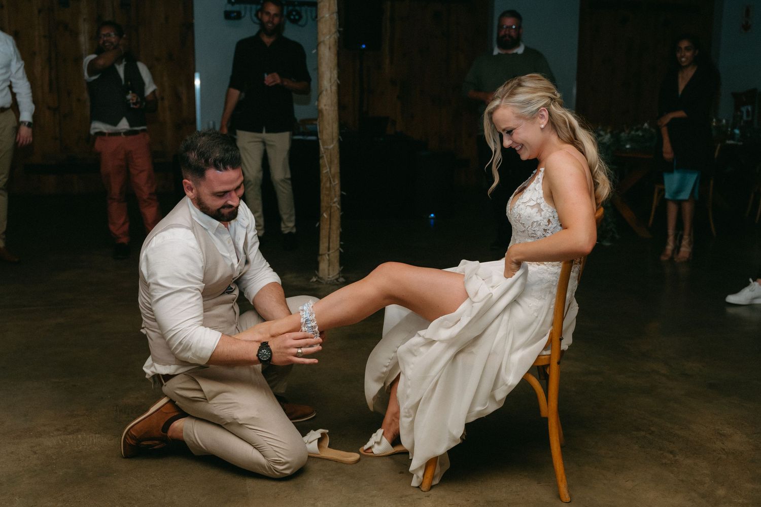 Couple participates in wedding shoe game during reception under string lights.