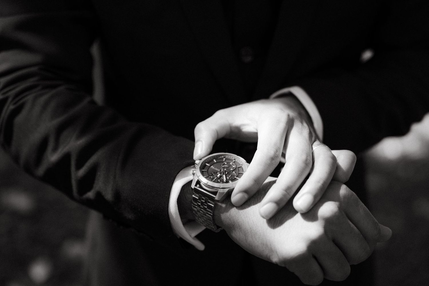 Black and white closeup of hands checking time on a luxury wrist watch.
