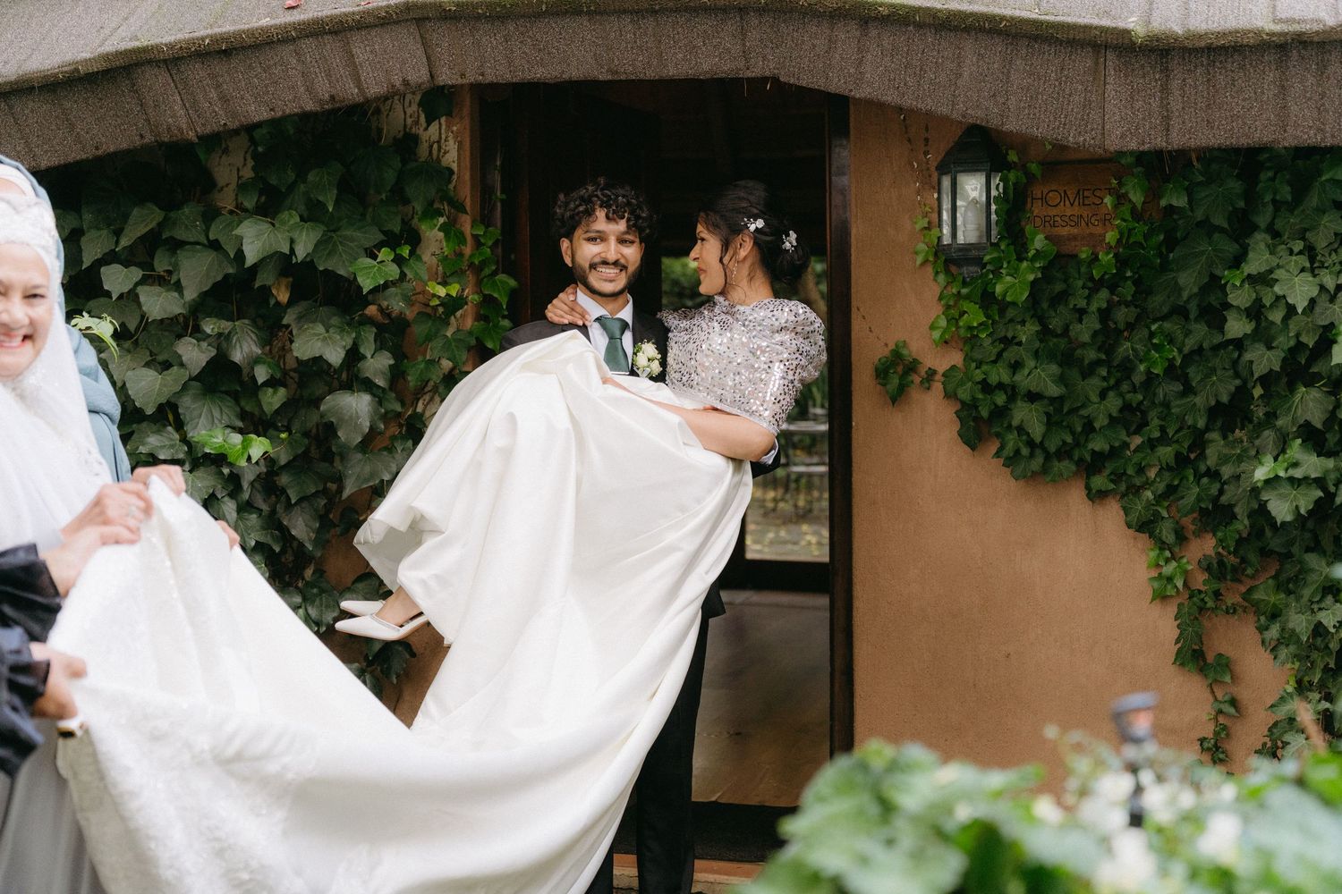 Wedding couple shares joyful moments in a garden setting with trailing greenery and white dress details.