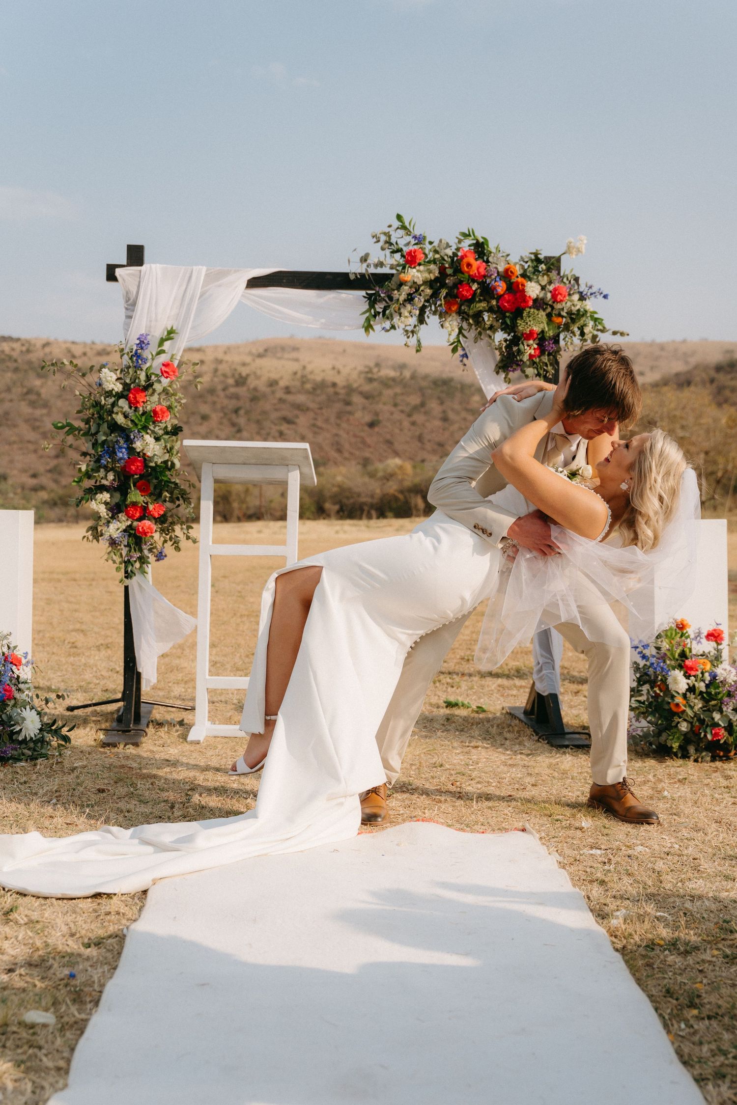Wedding ceremony setup with white chairs and floral arrangements in an outdoor desert setting.