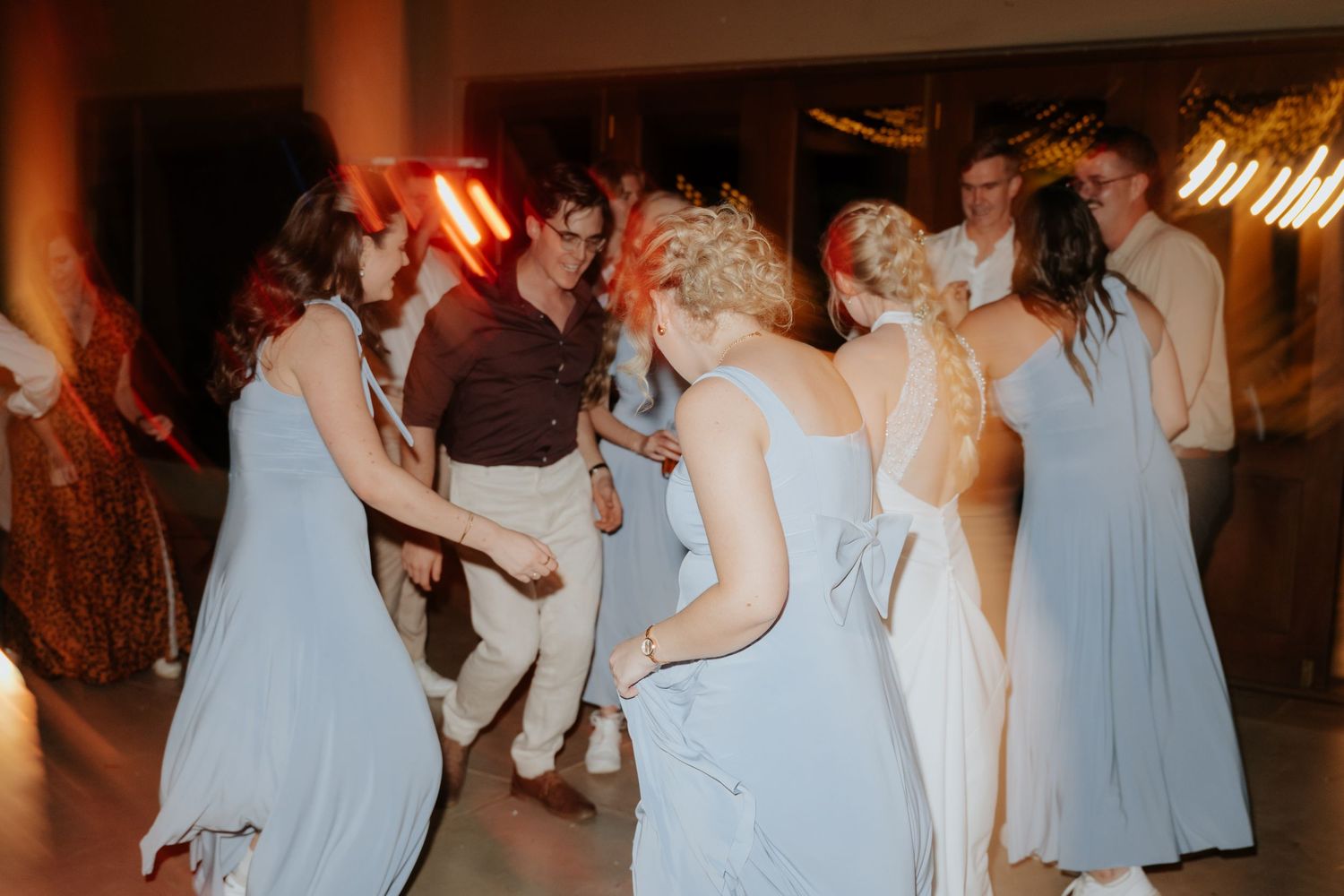 Wedding guests in light blue bridesmaid dresses dancing together during an evening reception celebration.