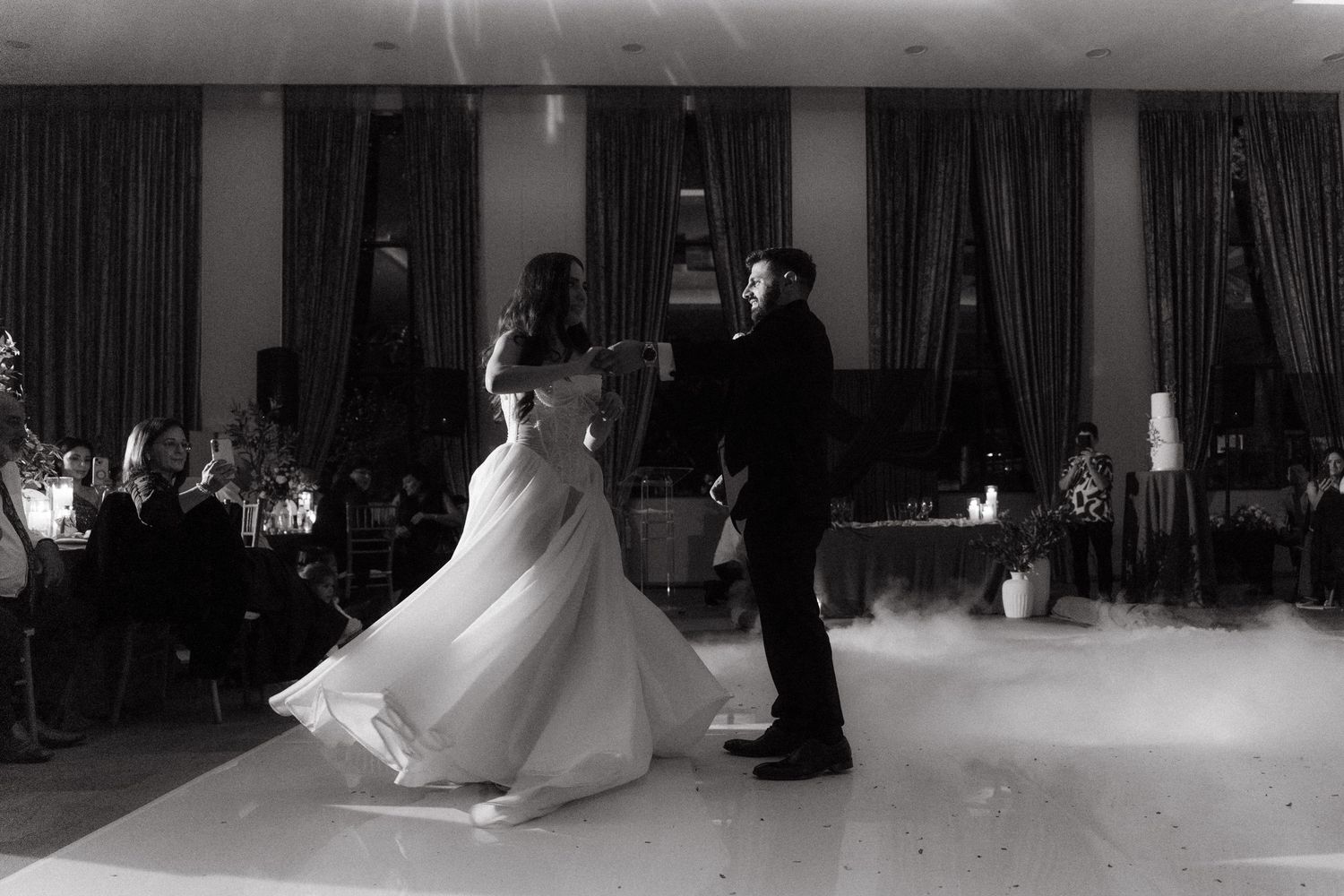 Black and white photo of a bride and groom sharing their first dance on a foggy dance floor at their wedding reception.
