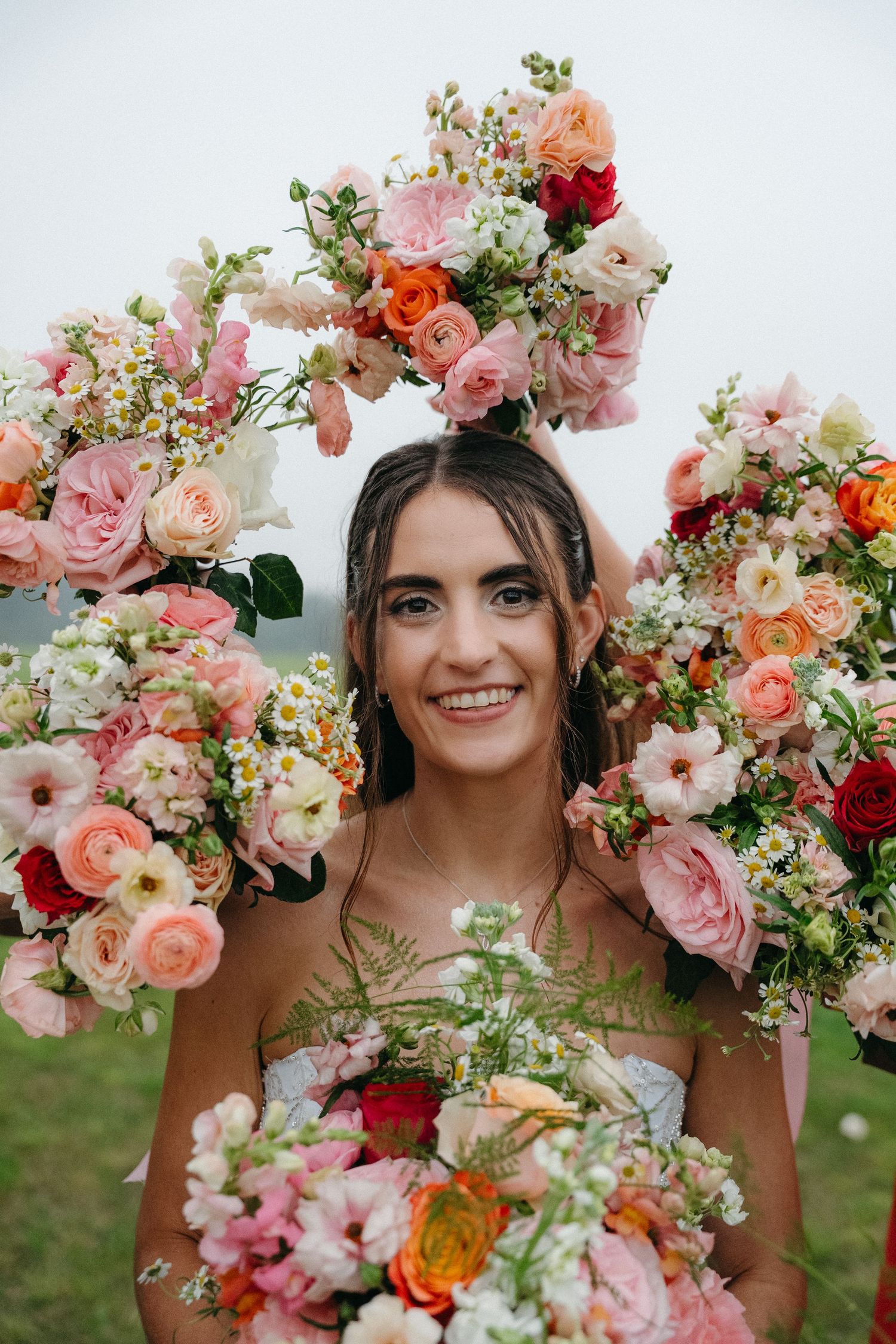 Smiling bride surrounded by a circular arch of colorful pink, red, and orange flowers, holding a bouquet.