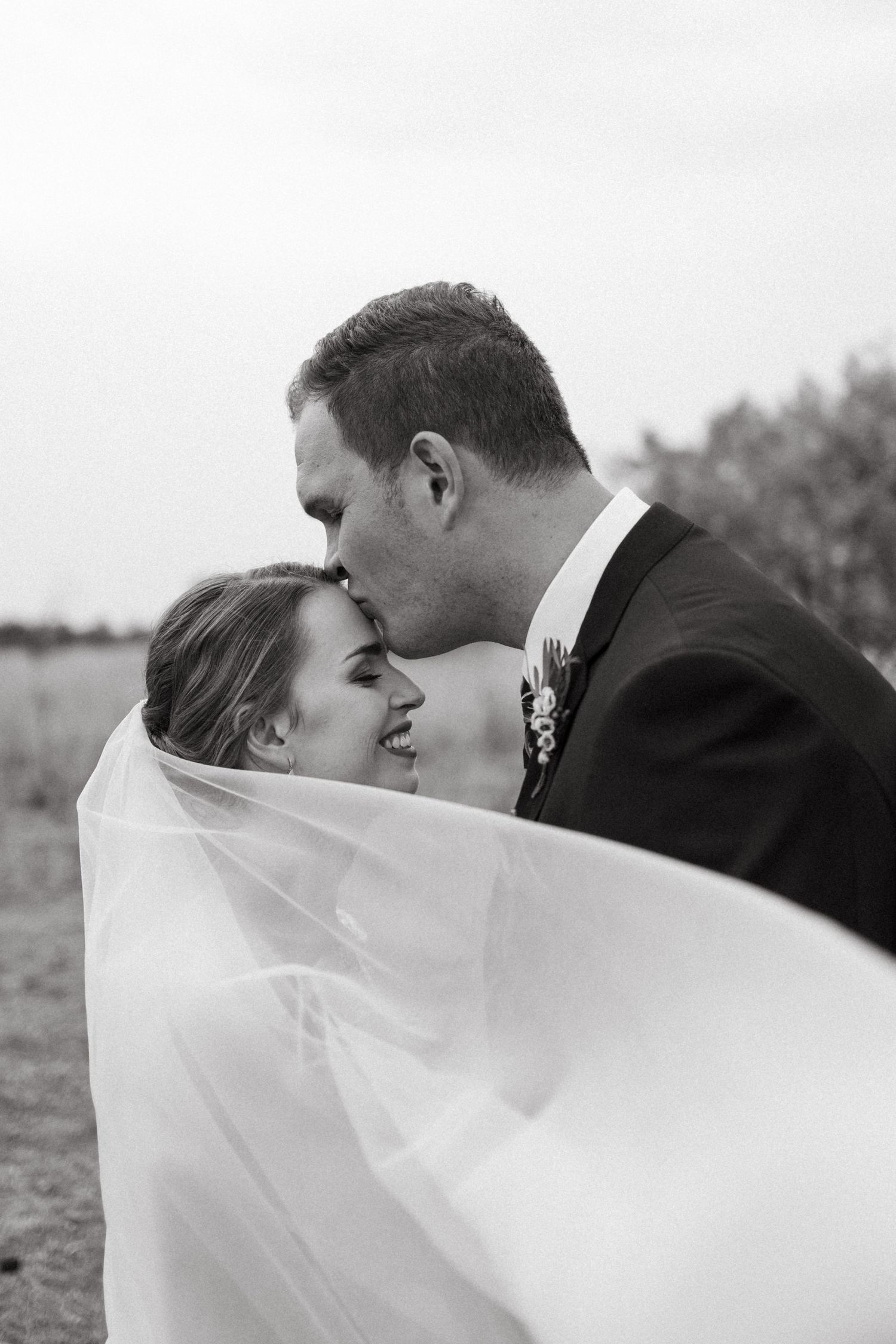 Romantic black and white portrait of newlyweds sharing intimate moment with flowing veil.