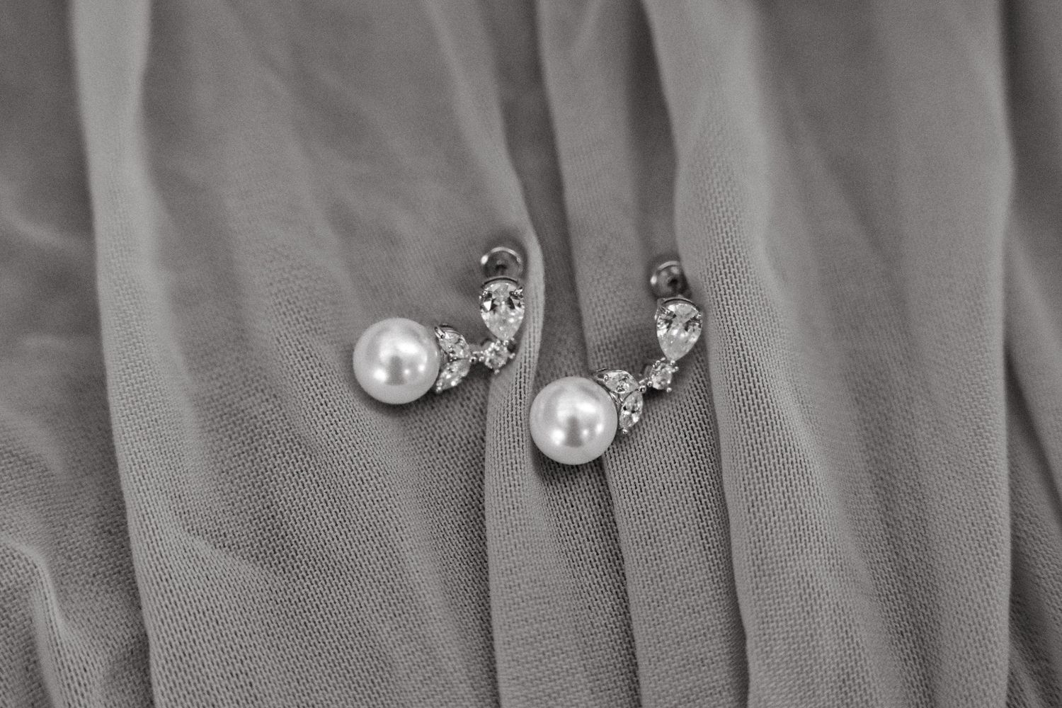 A close-up view of silver and pearl stud earrings arranged in a row against a gray fabric background.