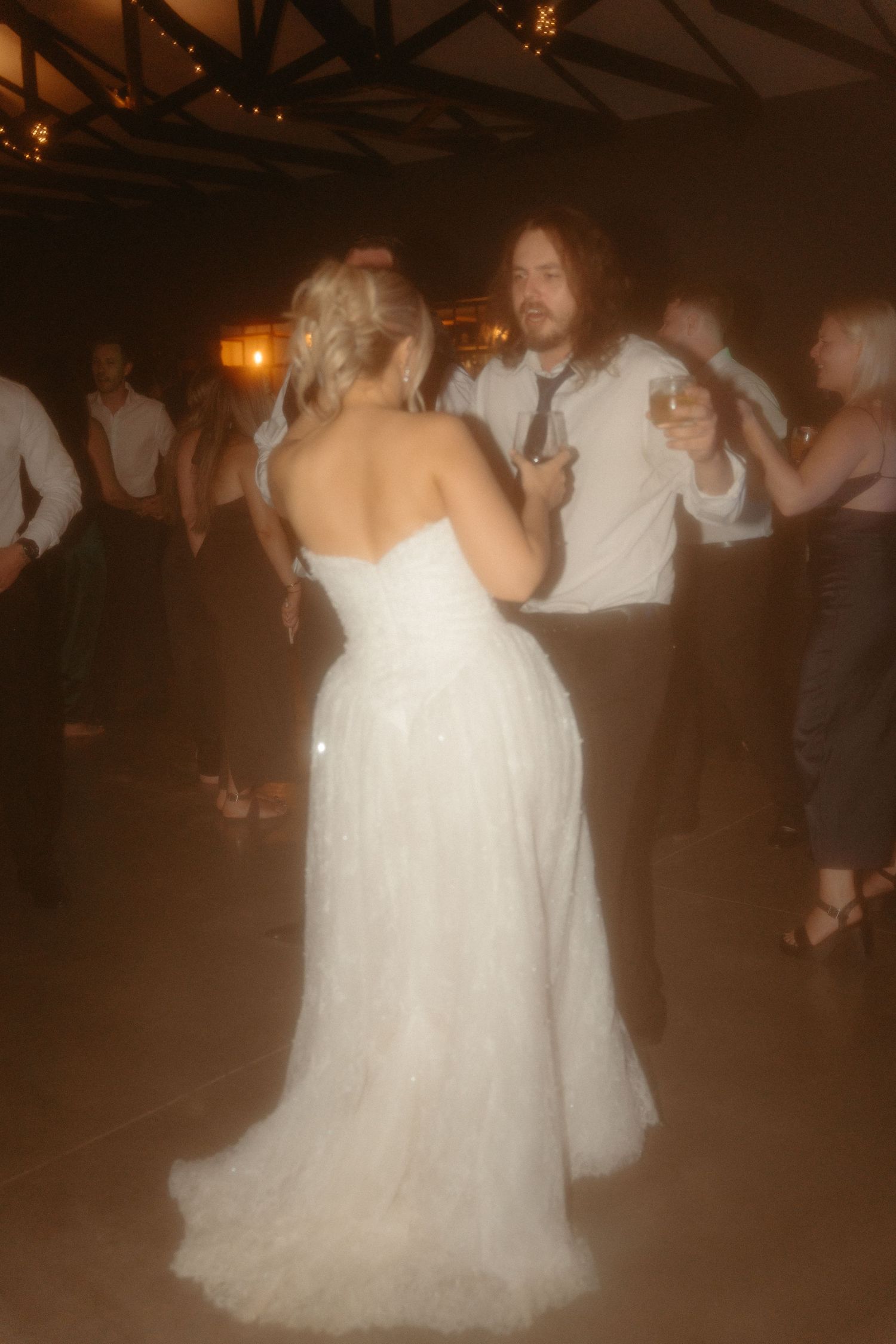 People dancing at a wedding reception with a bride in a white gown on a dimly lit dance floor.