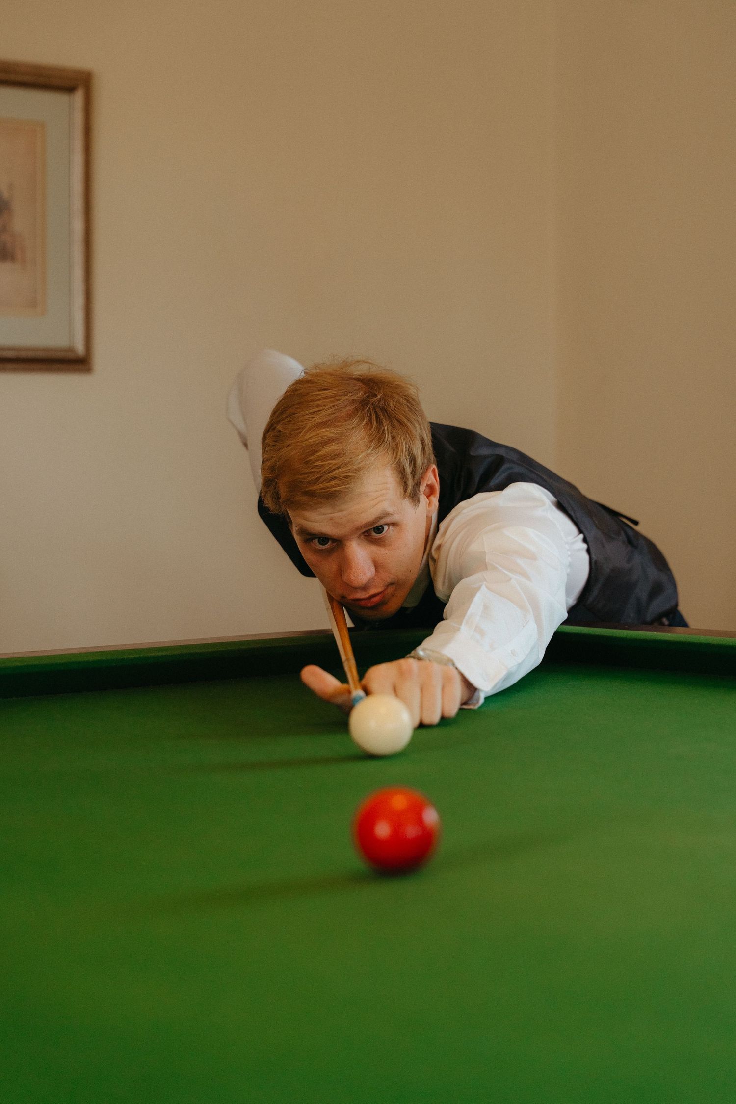 A player leans over a green snooker table, preparing to take a shot at the red ball.