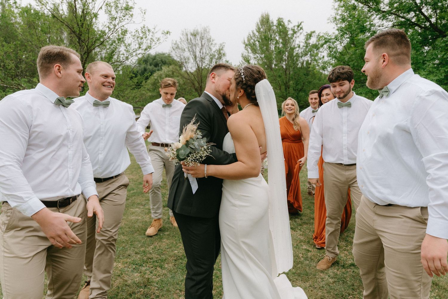 Wedding party celebrating with joyful dance moves in an outdoor garden setting.