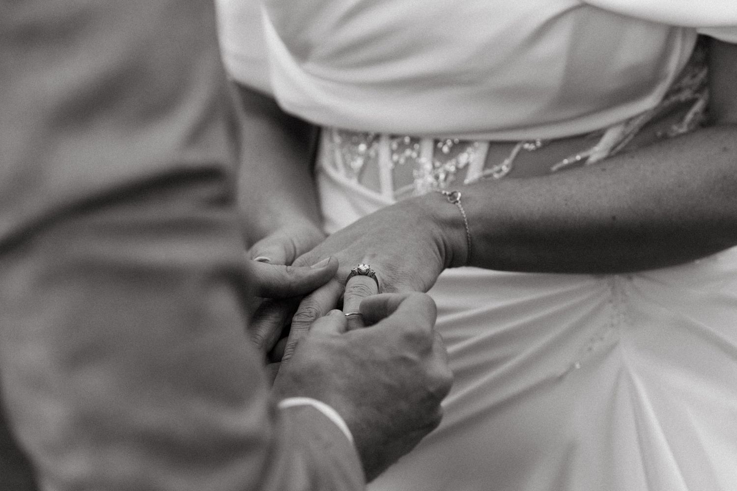 Black and white detail shot of hands exchanging wedding rings during ceremony.
