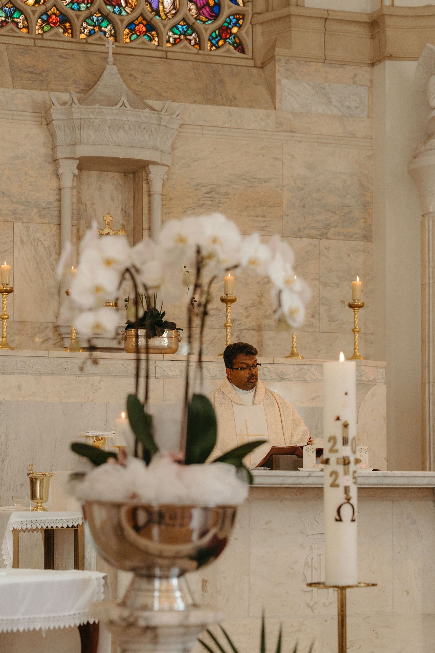 White orchids in silver bowl with ornate church altar and candles in elegant interior setting.