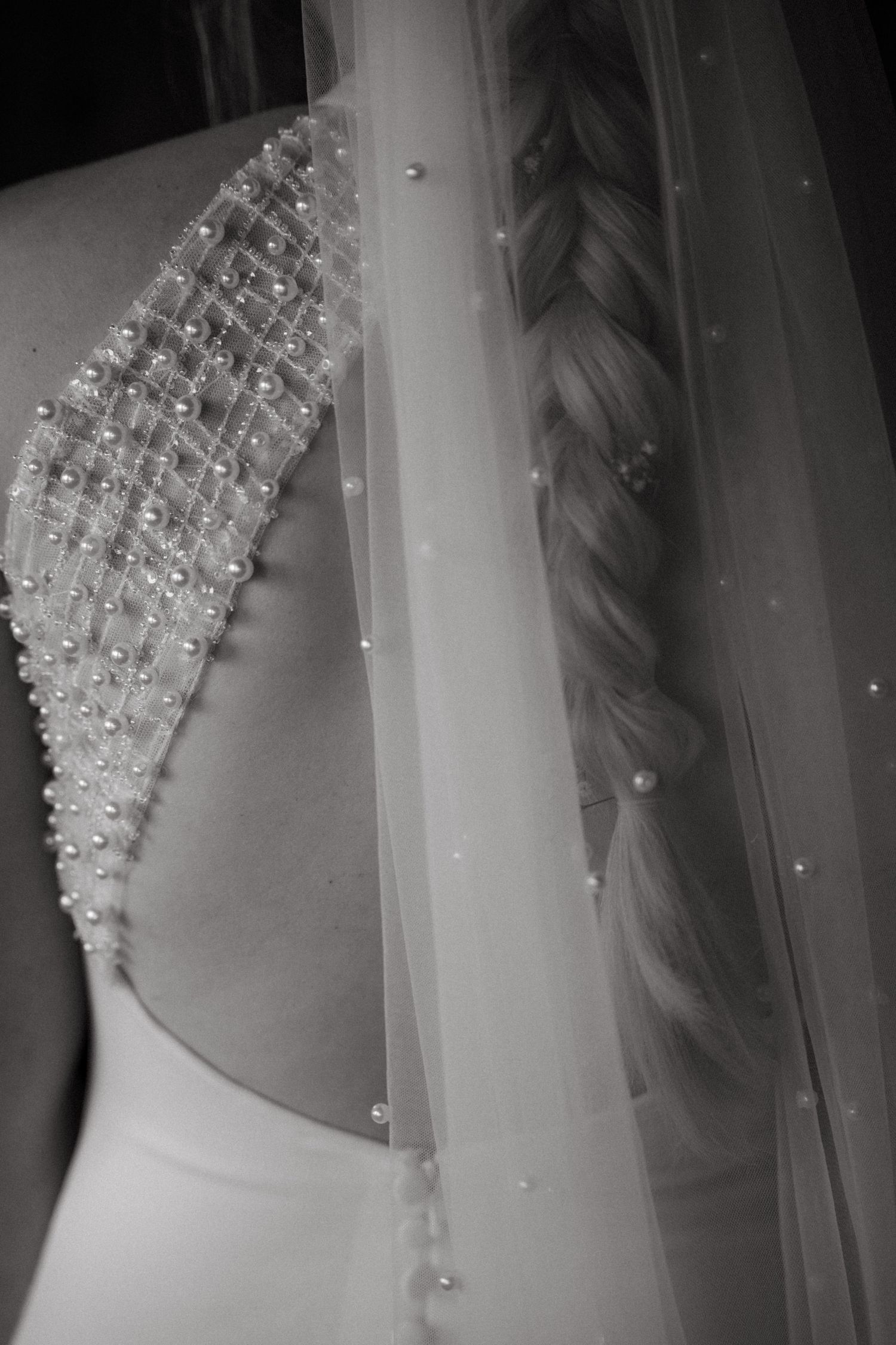 Black and white detail of a wedding dress showing beaded shoulder embellishment and delicate veil with pearls.