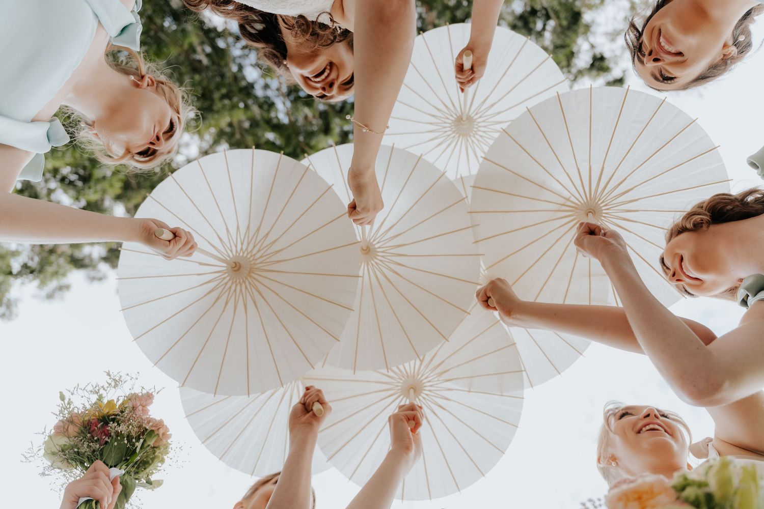 A group of people holding white paper parasols in a circle formation, viewed from below against a sunny sky.