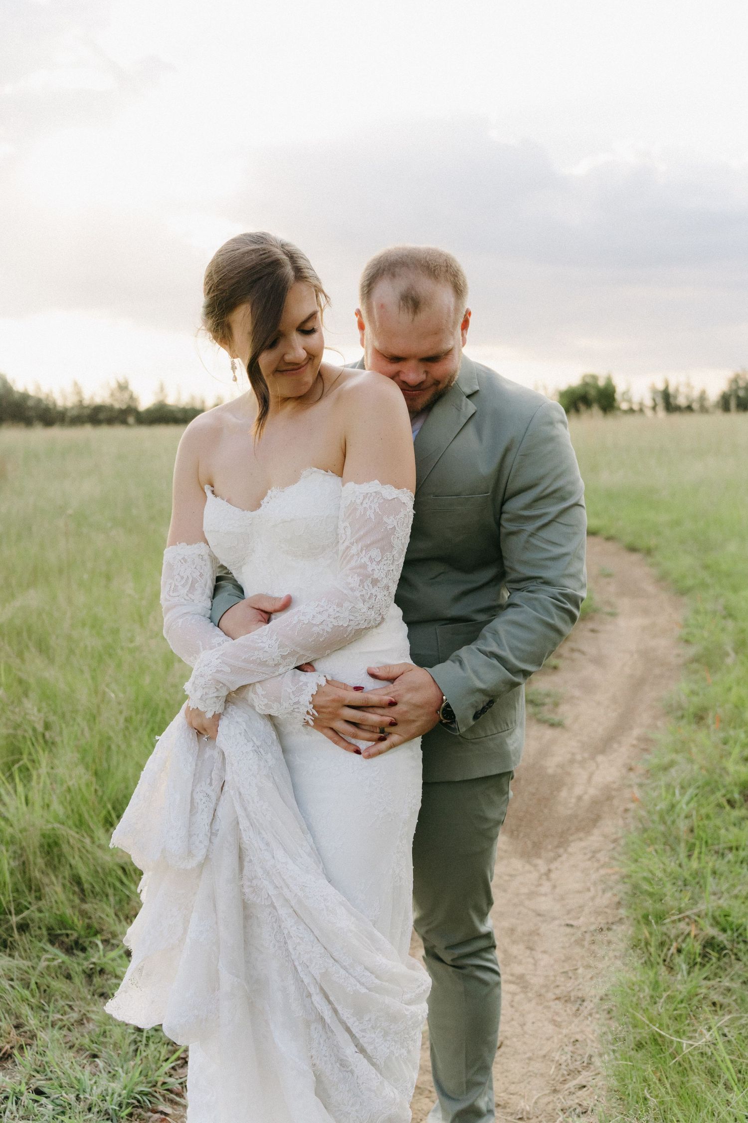 Romantic moment between newlyweds on rustic dirt path in golden field at sunset.