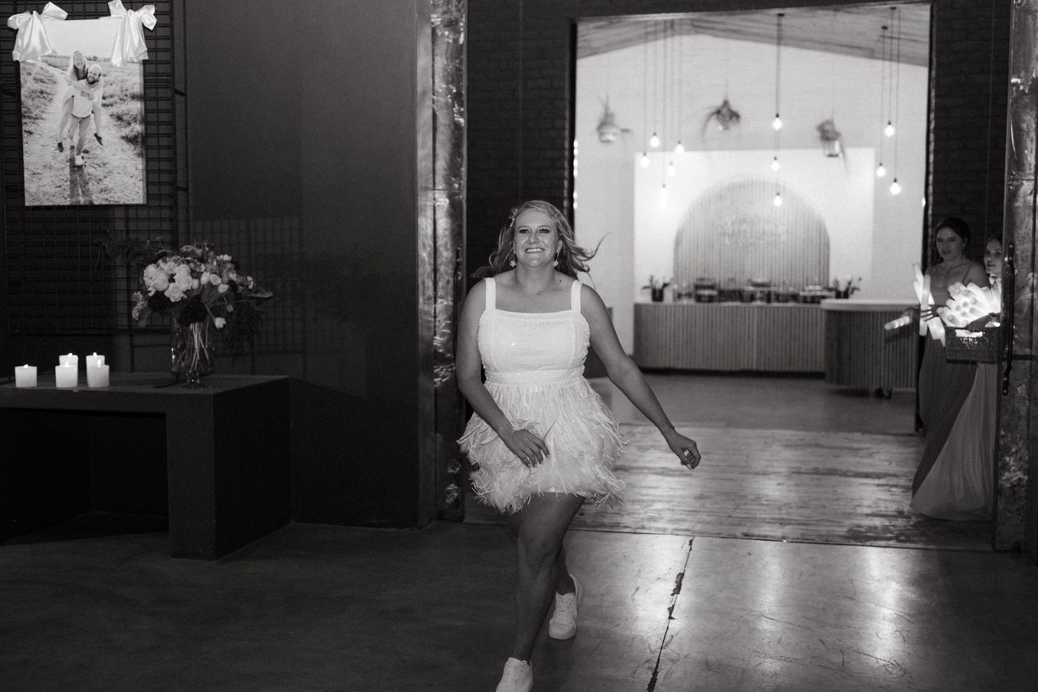 Black and white photo of someone dancing in a short dress at a wedding reception venue.