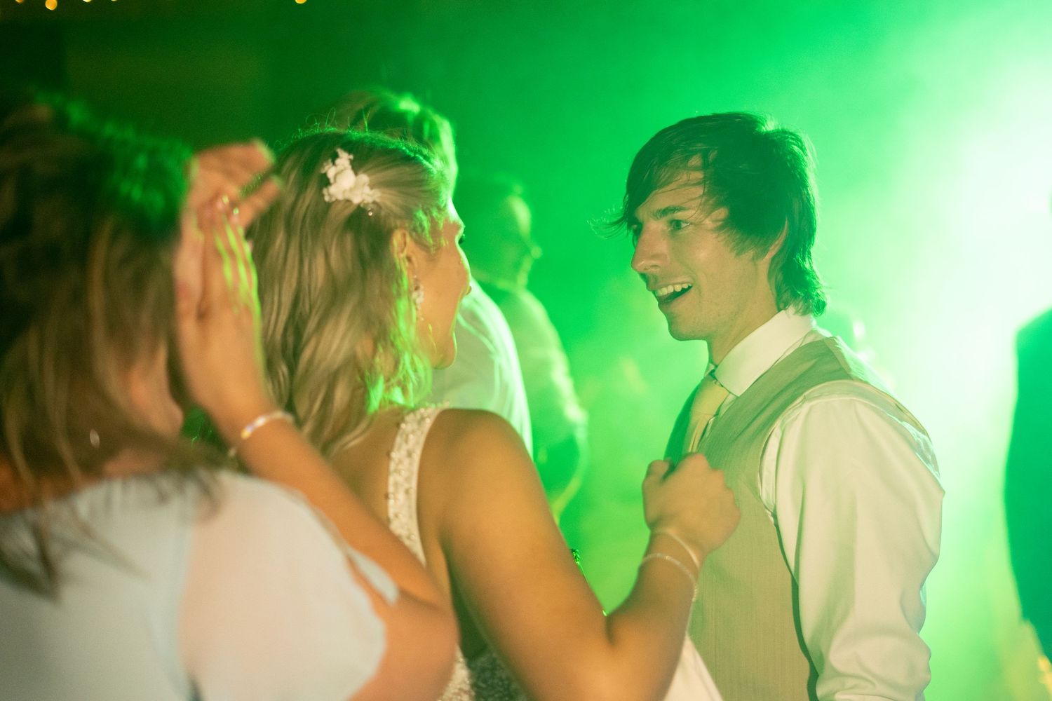 Dance floor scene bathed in green lighting at a wedding reception.