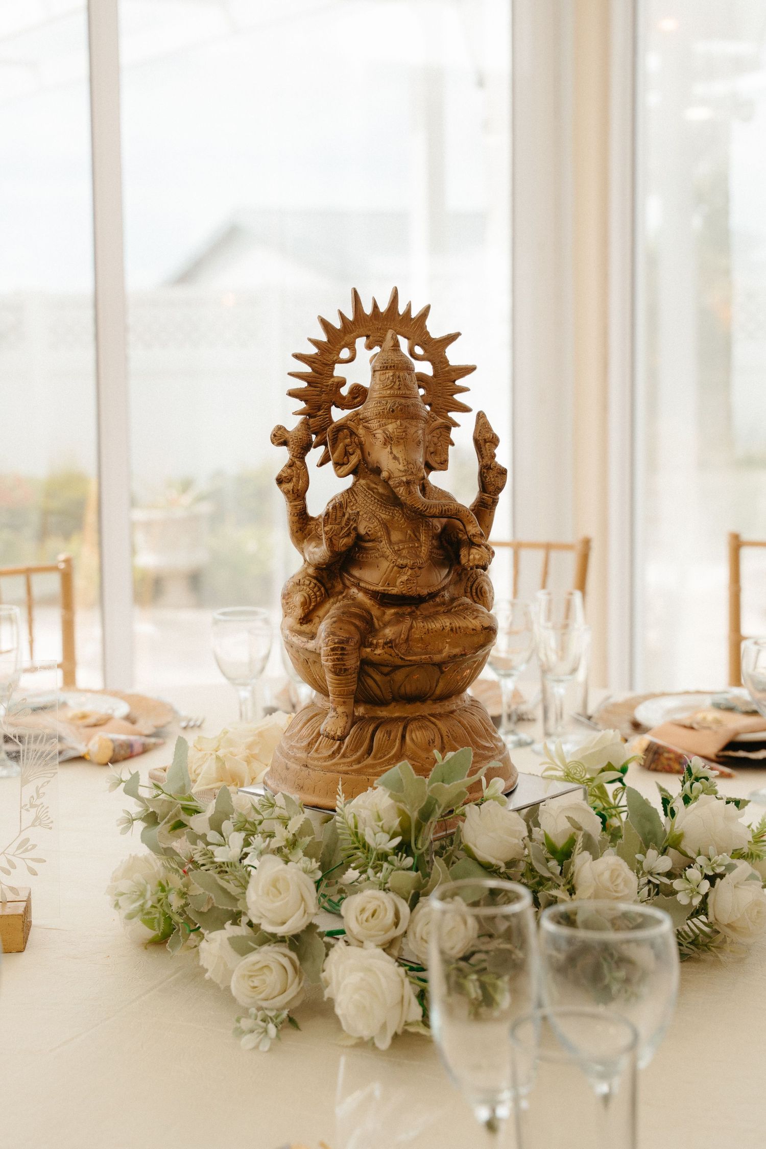 Elegant wedding table Hindu centerpiece featuring gold sculptures and white floral arrangements with greenery.