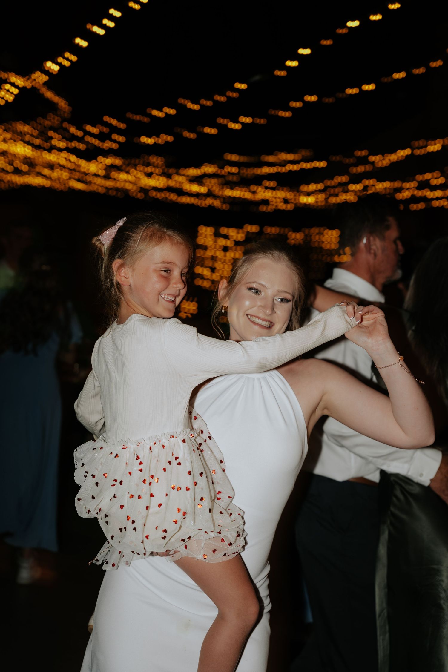 Wedding couple dancing under warm string lights at their reception.