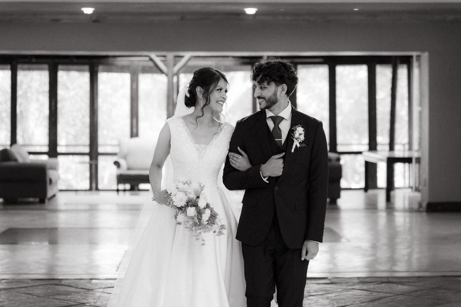 Black and white photo of newlyweds sharing a tender moment in an elegant indoor venue.