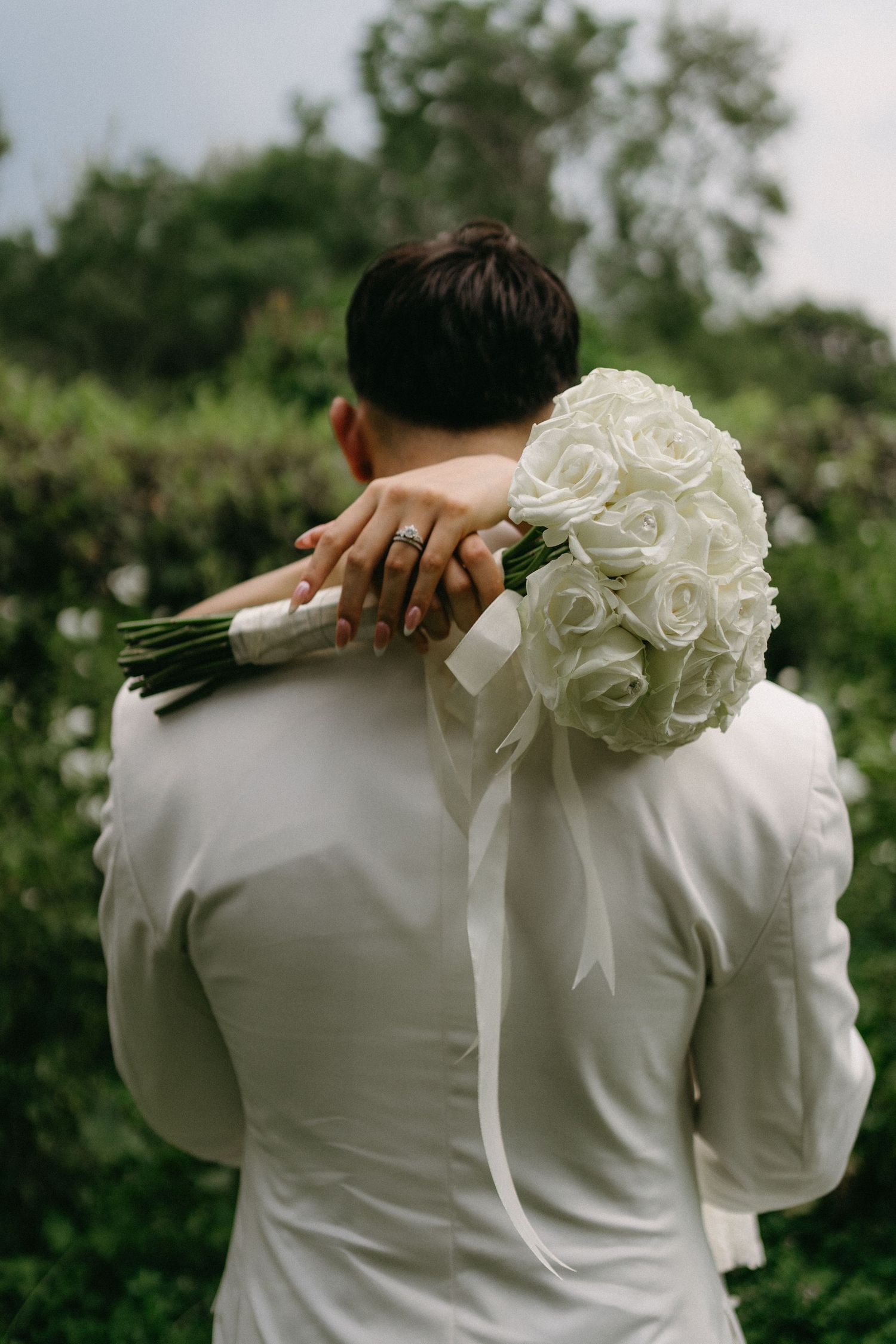 A romantic wedding detail shot showing a white rose bouquet held against a person in white attire.